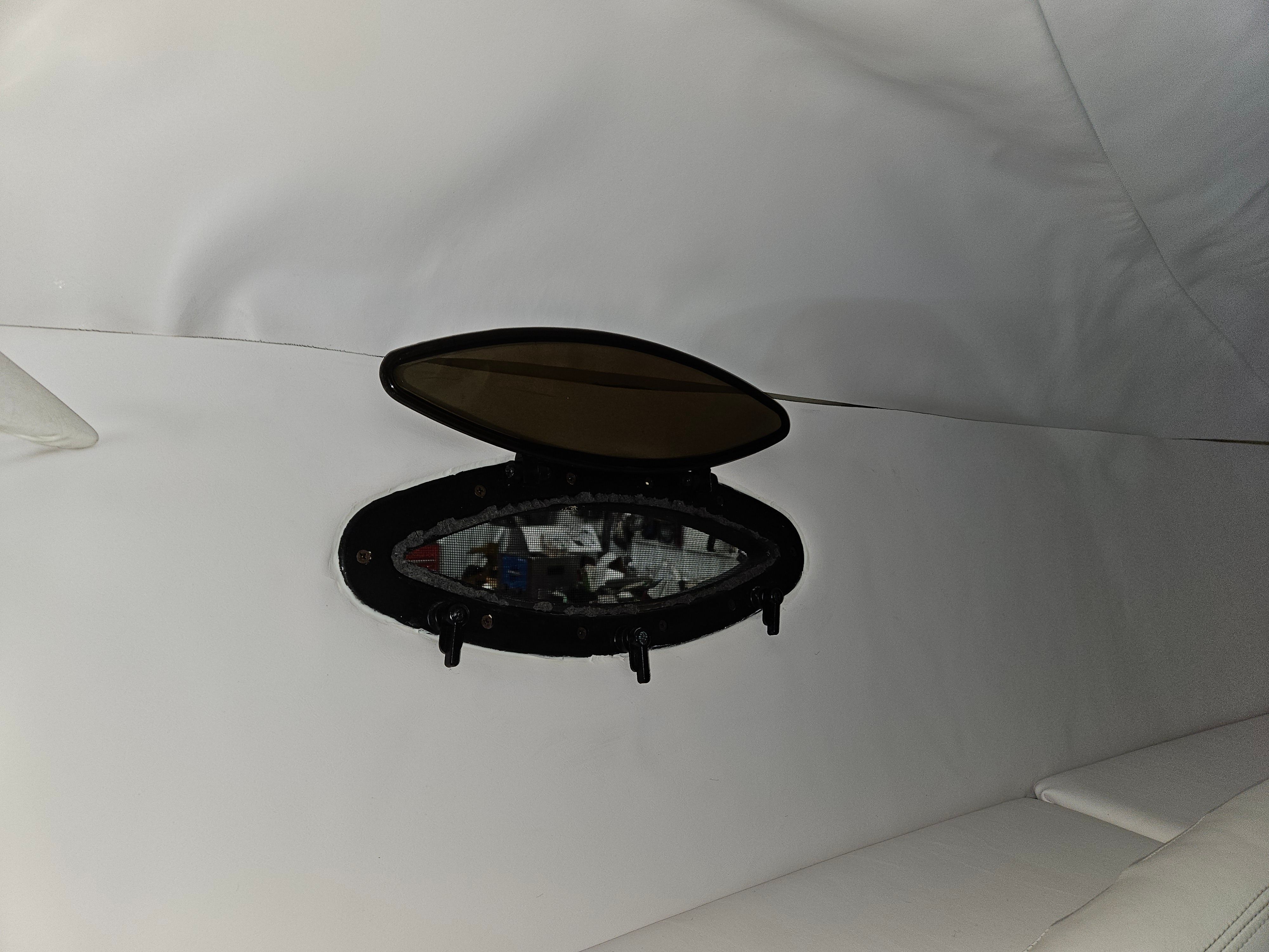 A small, oval porthole in a white interior wall of a boat.