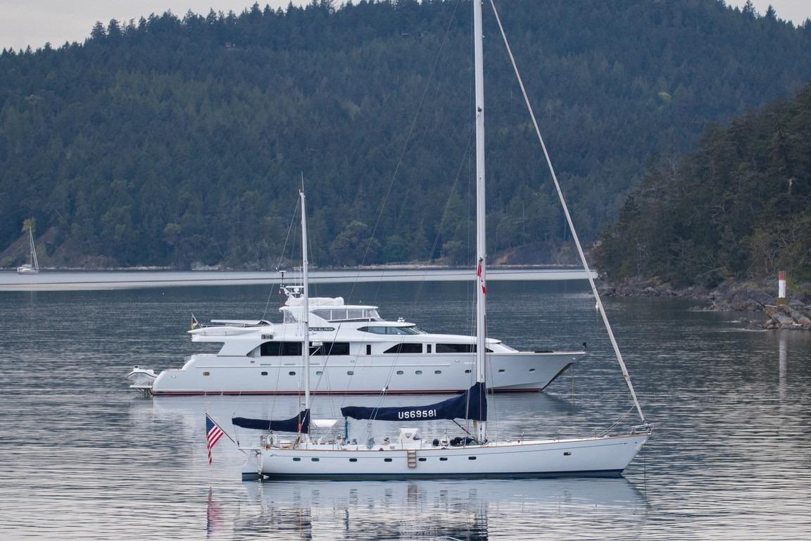 Sailboats on calm water with forested hills, featuring a 1968 Abeking & Rasmussen Tripp 74.