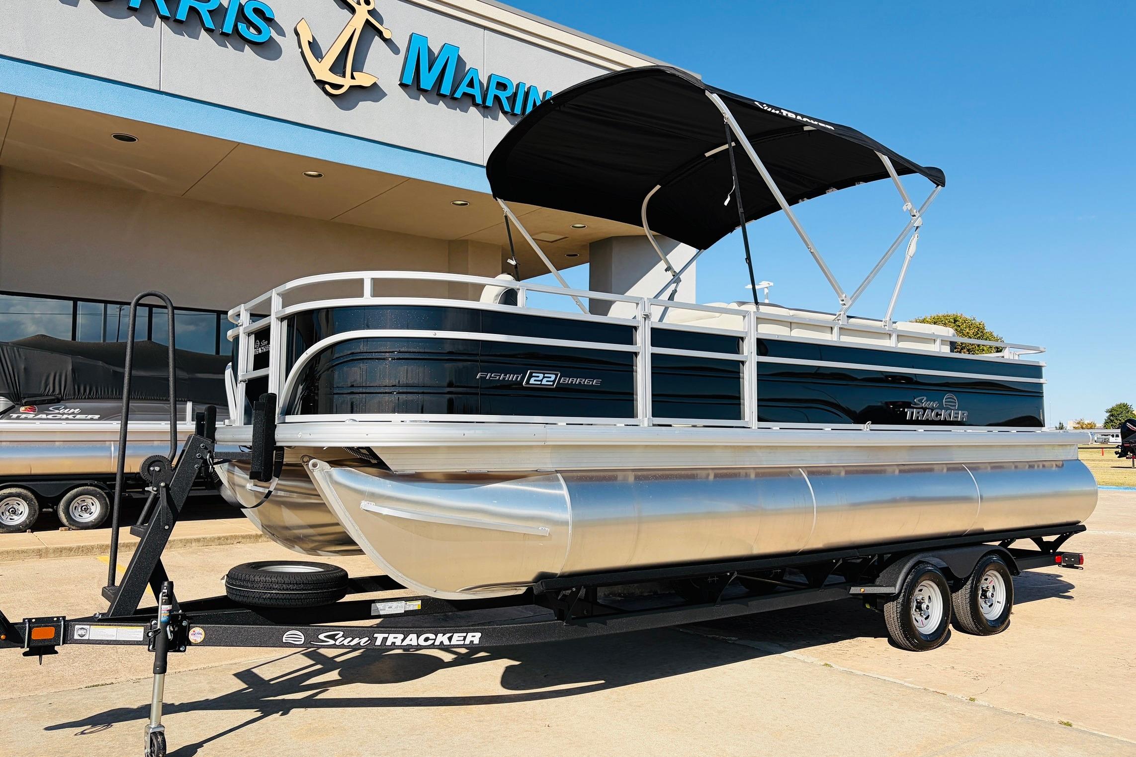 2026 Sun Tracker Fishin' Barge 22 XP3 pontoon boat on trailer outside dealership.