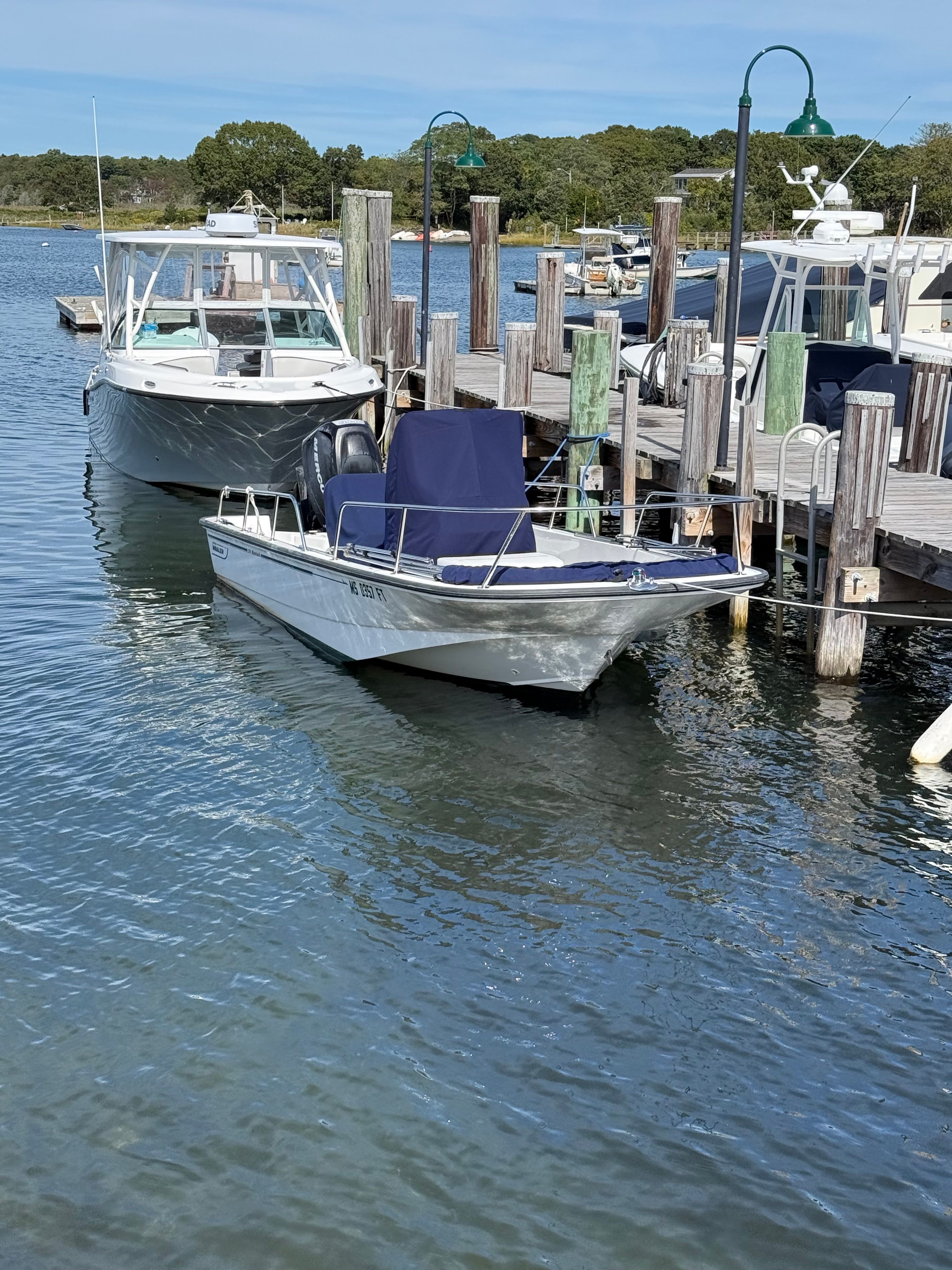 A 2011 Boston Whaler 170 Montauk is docked at a wooden pier in a calm harbor.