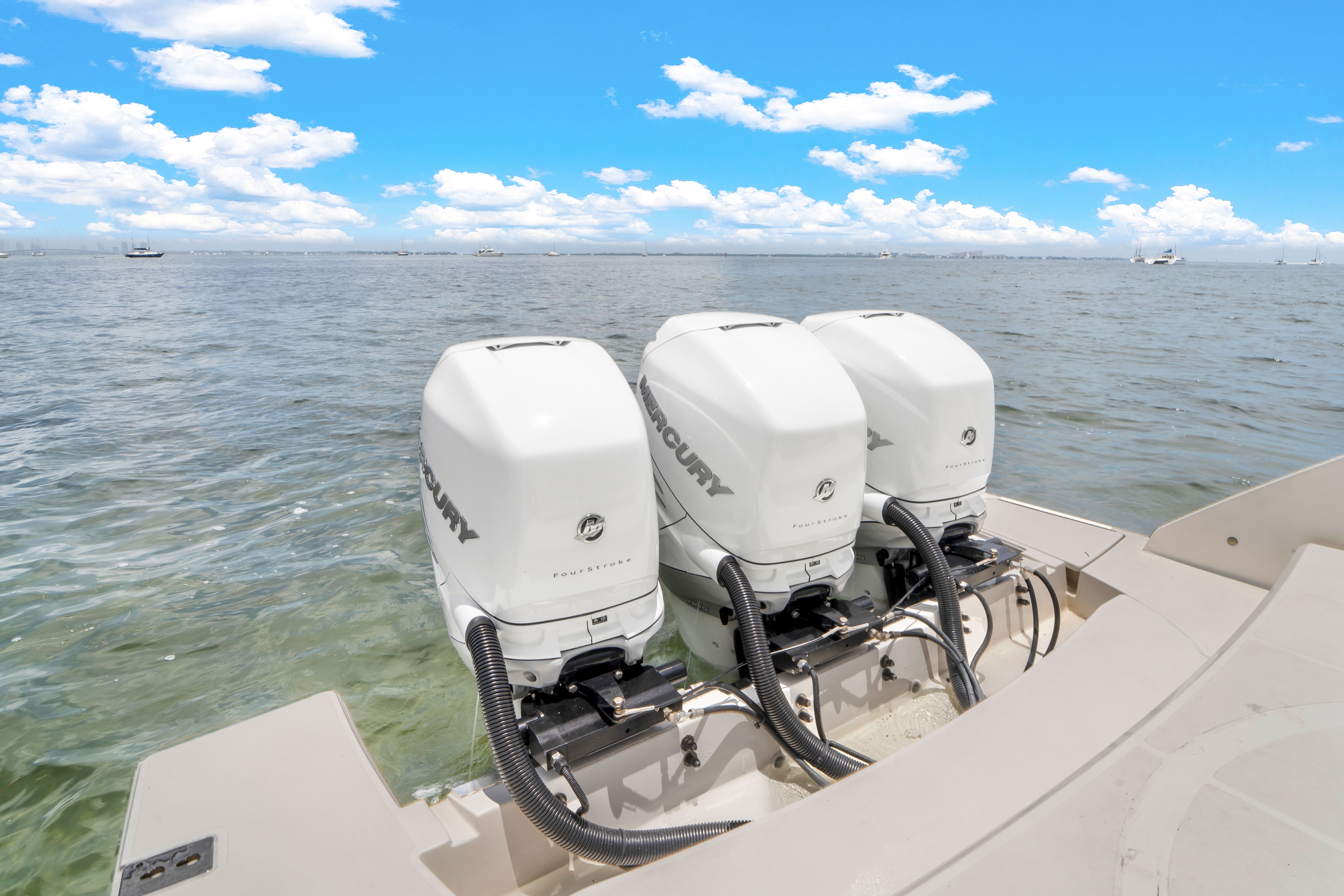 Three outboard engines on a boat in calm waters under a blue sky.