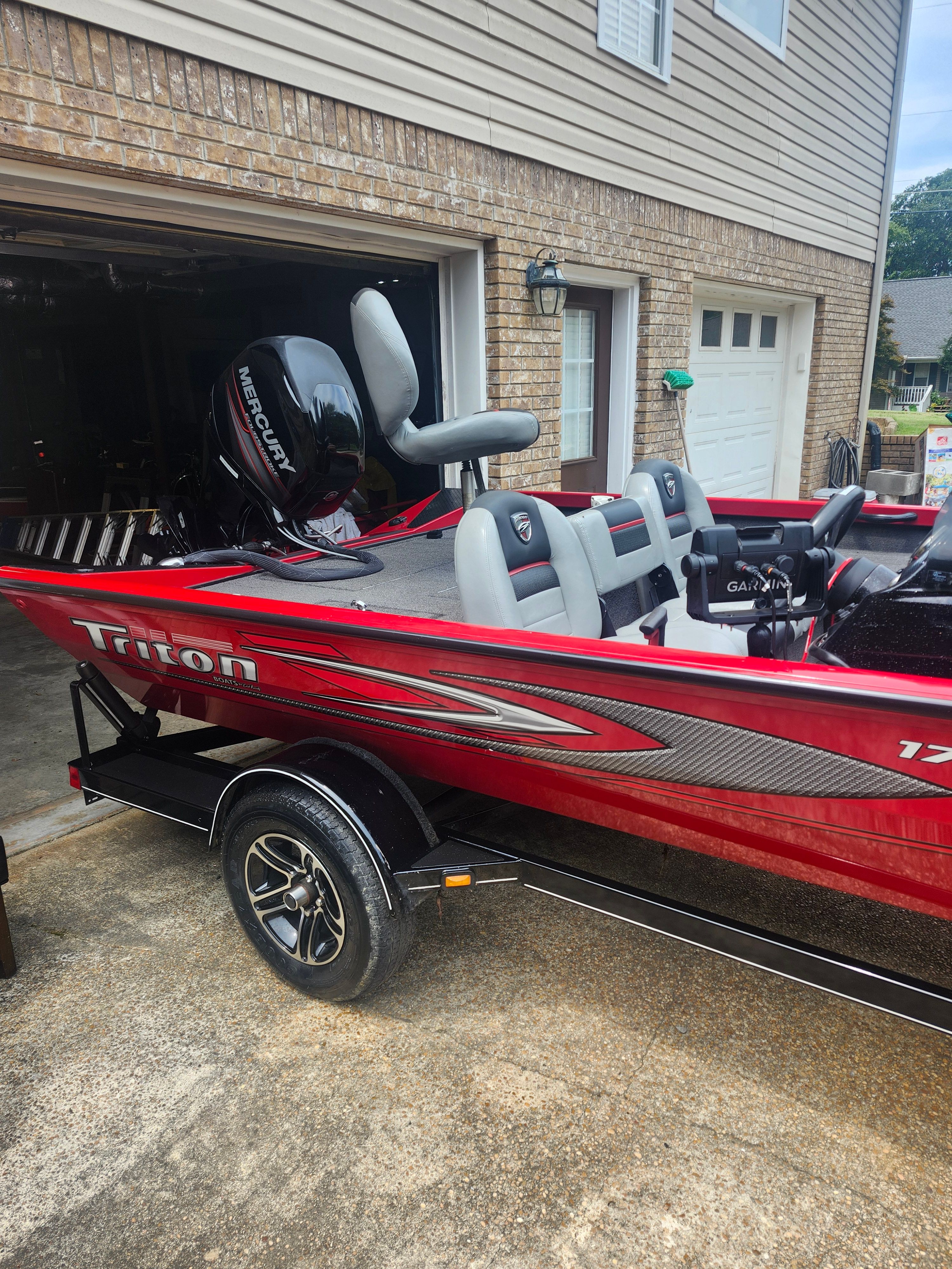A red 2015 Triton 17 C TX boat on a trailer in front of a garage.
