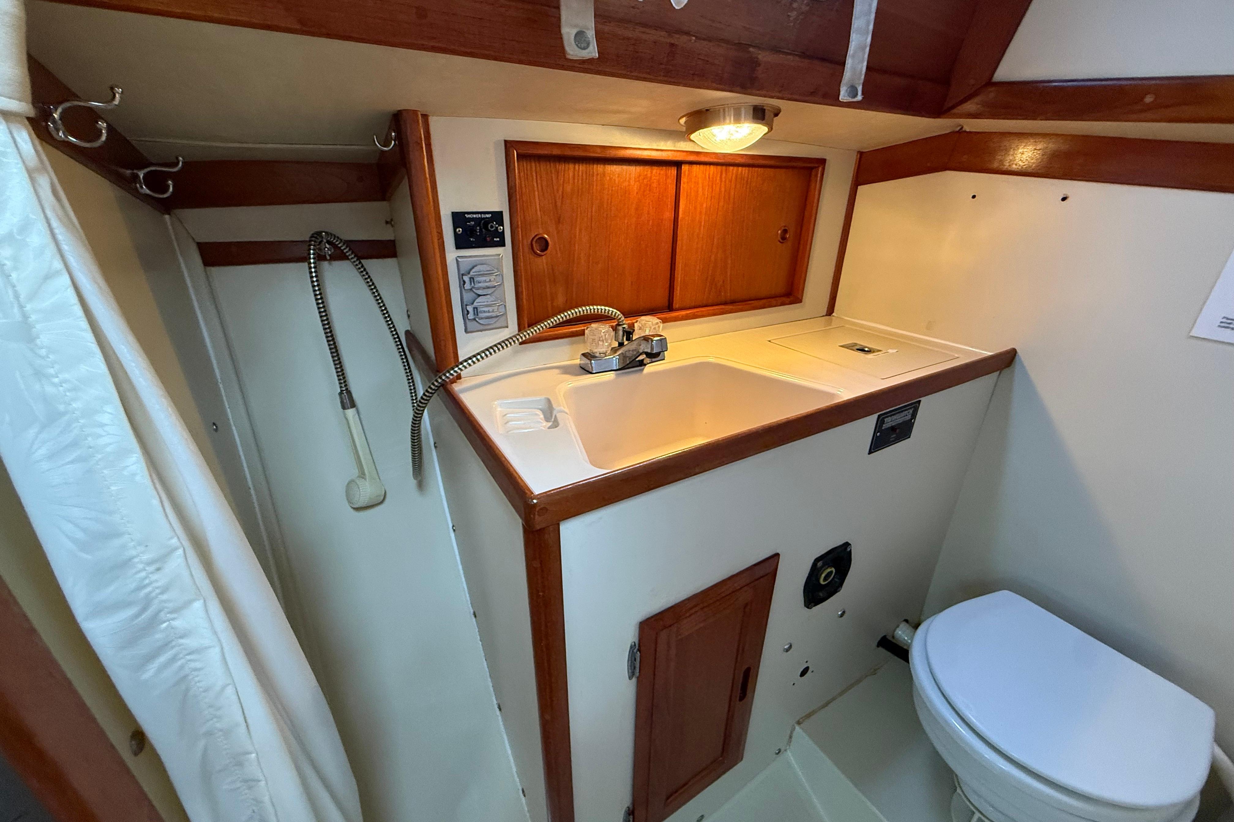 Compact bathroom in 1988 Ericson 32-200 sailboat with sink, toilet, and wooden cabinetry.