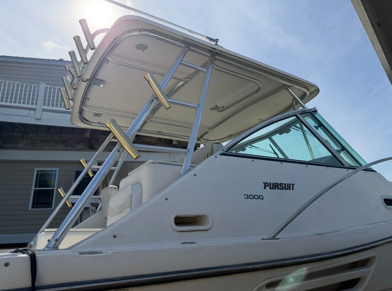 A 2002 Pursuit 3000 Express with a sturdy hardtop and fishing rod holders, parked near a building.