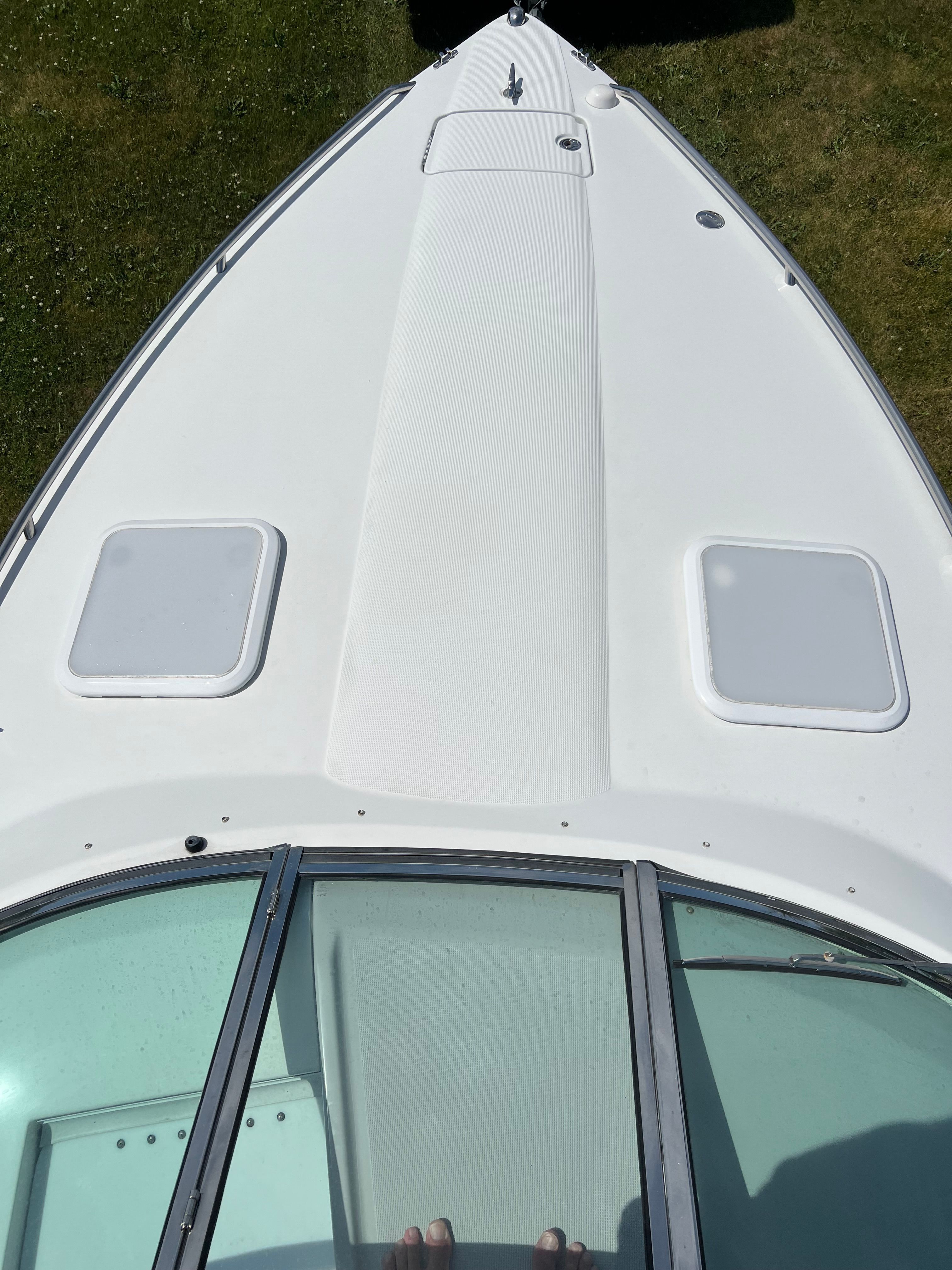 The image shows the foredeck of a white boat with two hatches and a windshield.