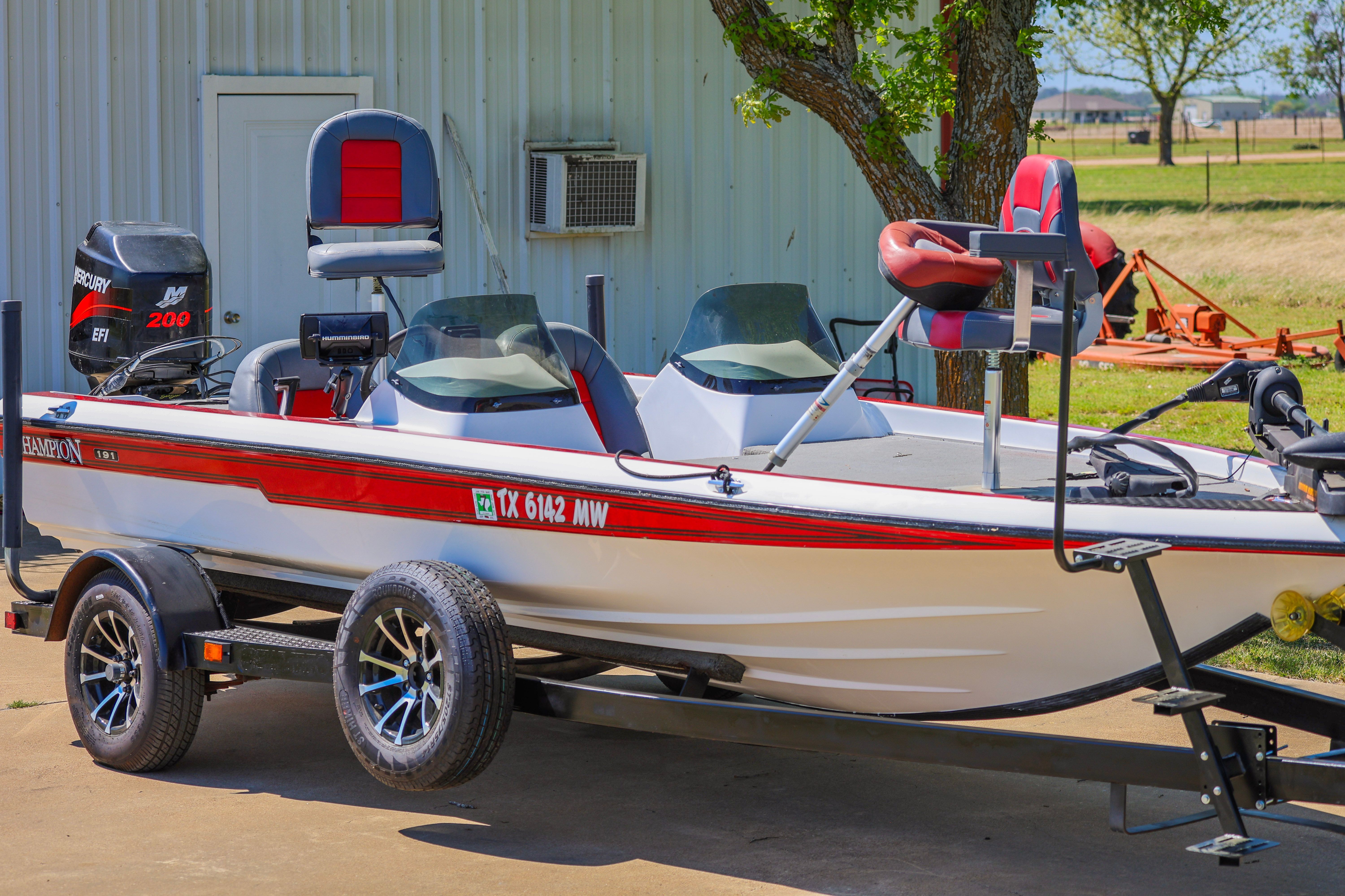 A 1999 Champion bass boat on a trailer, parked in front of a building.