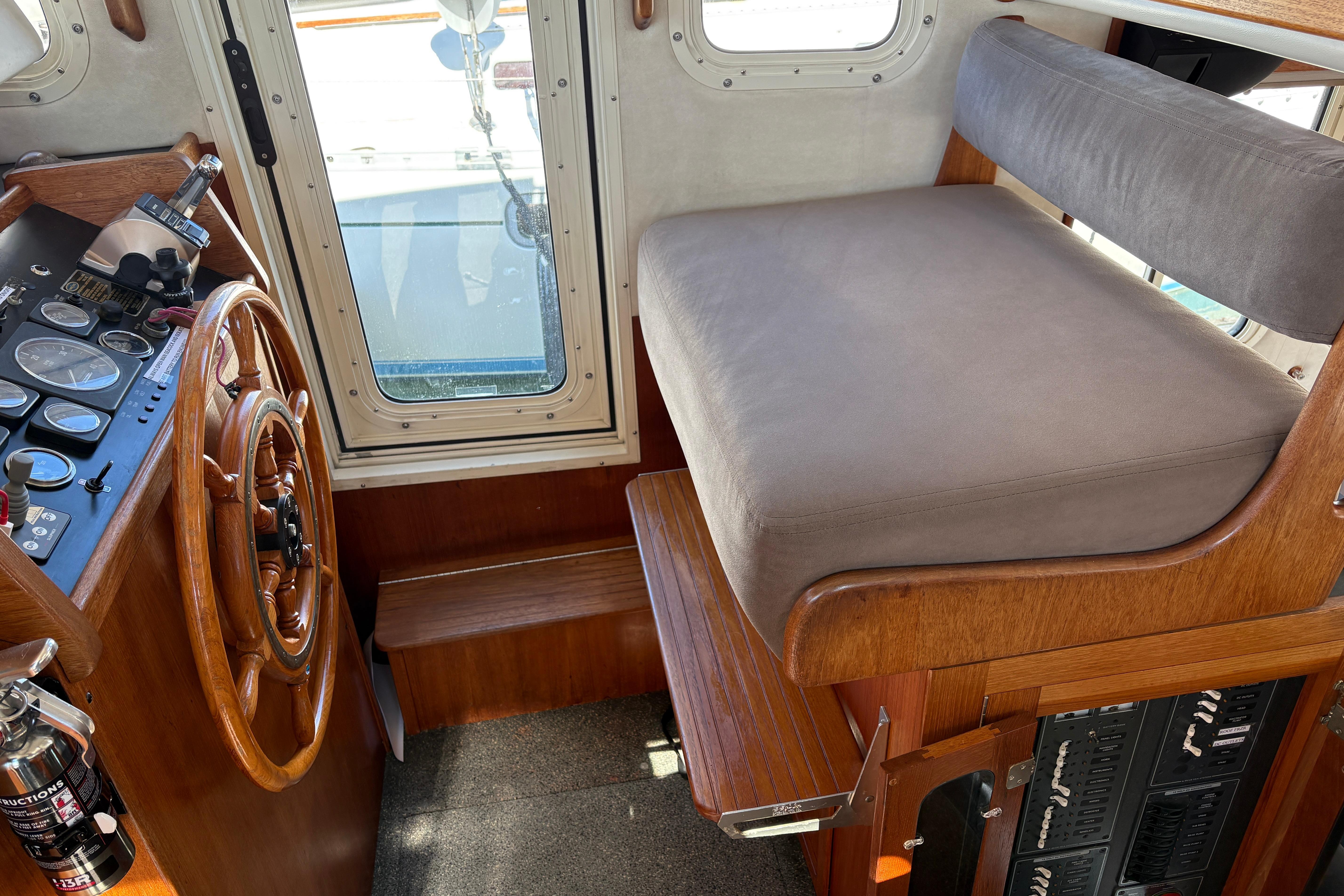 2004 Nordic Tug 32 interior helm with wooden steering wheel and cushioned seating.