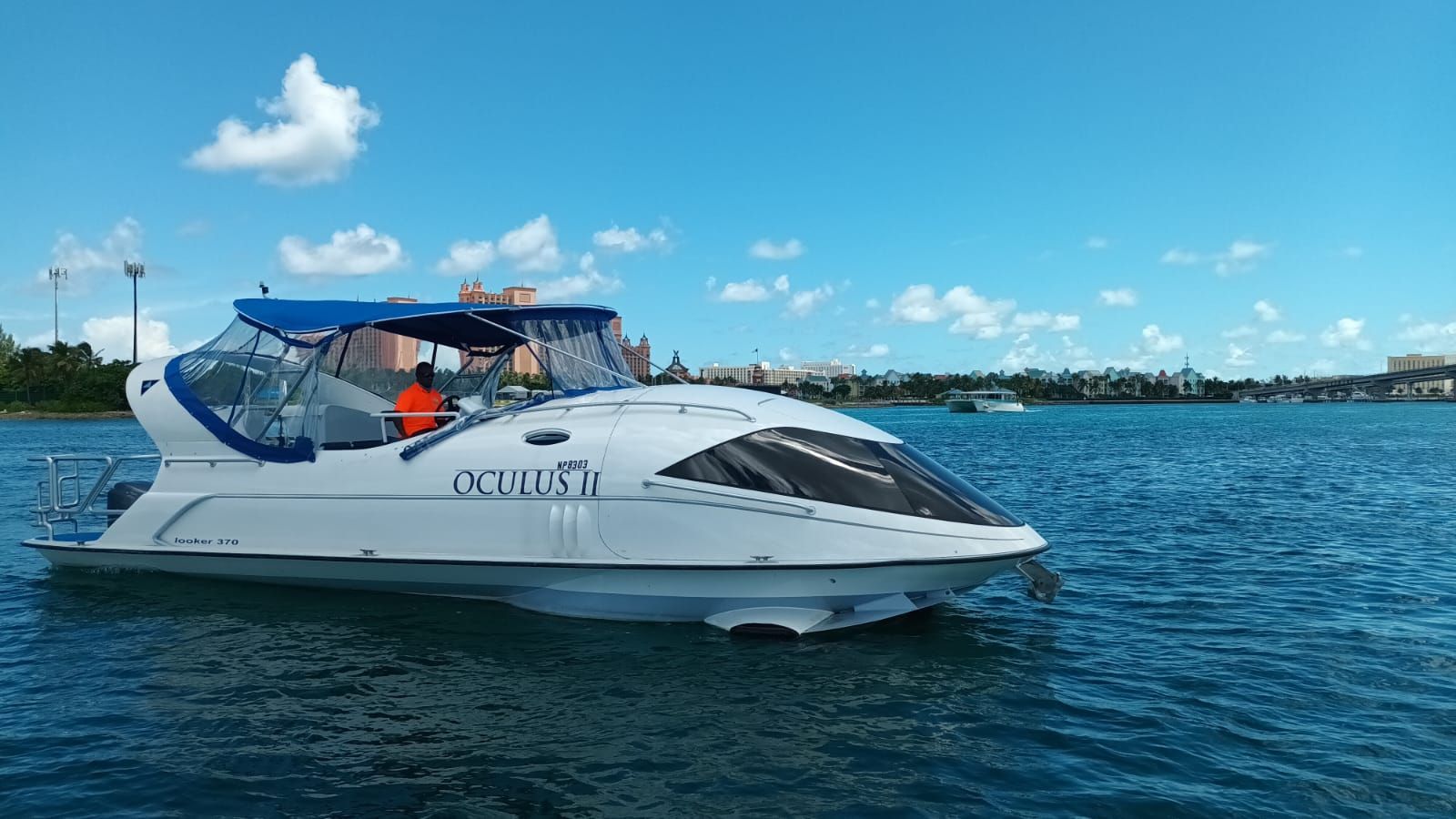 A modern boat with a glass roof cruises on calm water under a blue sky.