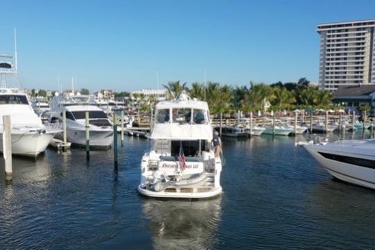 2005 Neptunus 56 Flybridge yacht navigating marina with palm trees and high-rise building.