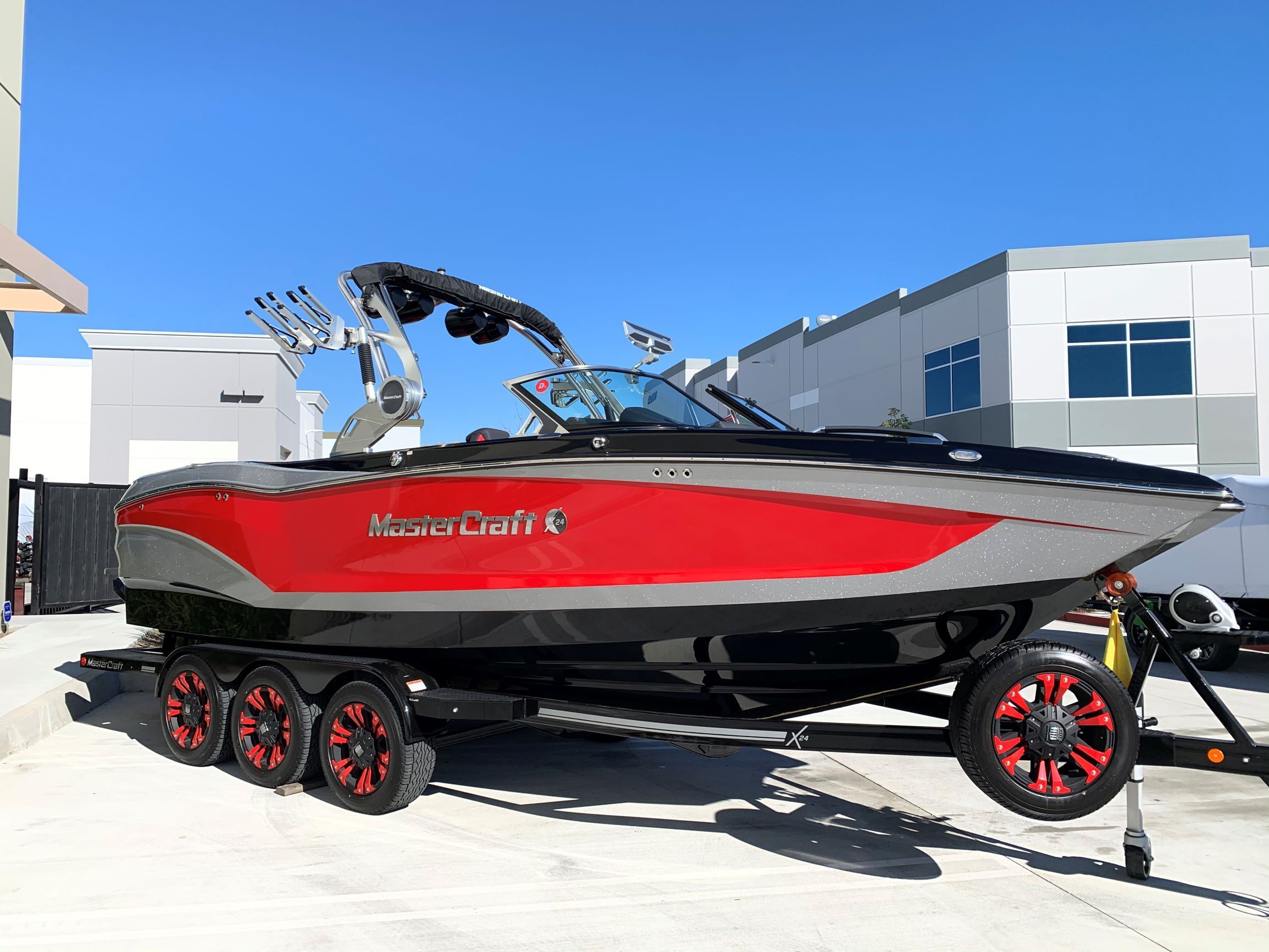 A 2020 MasterCraft X24 on a trailer, featuring a red and black design, parked in a lot.