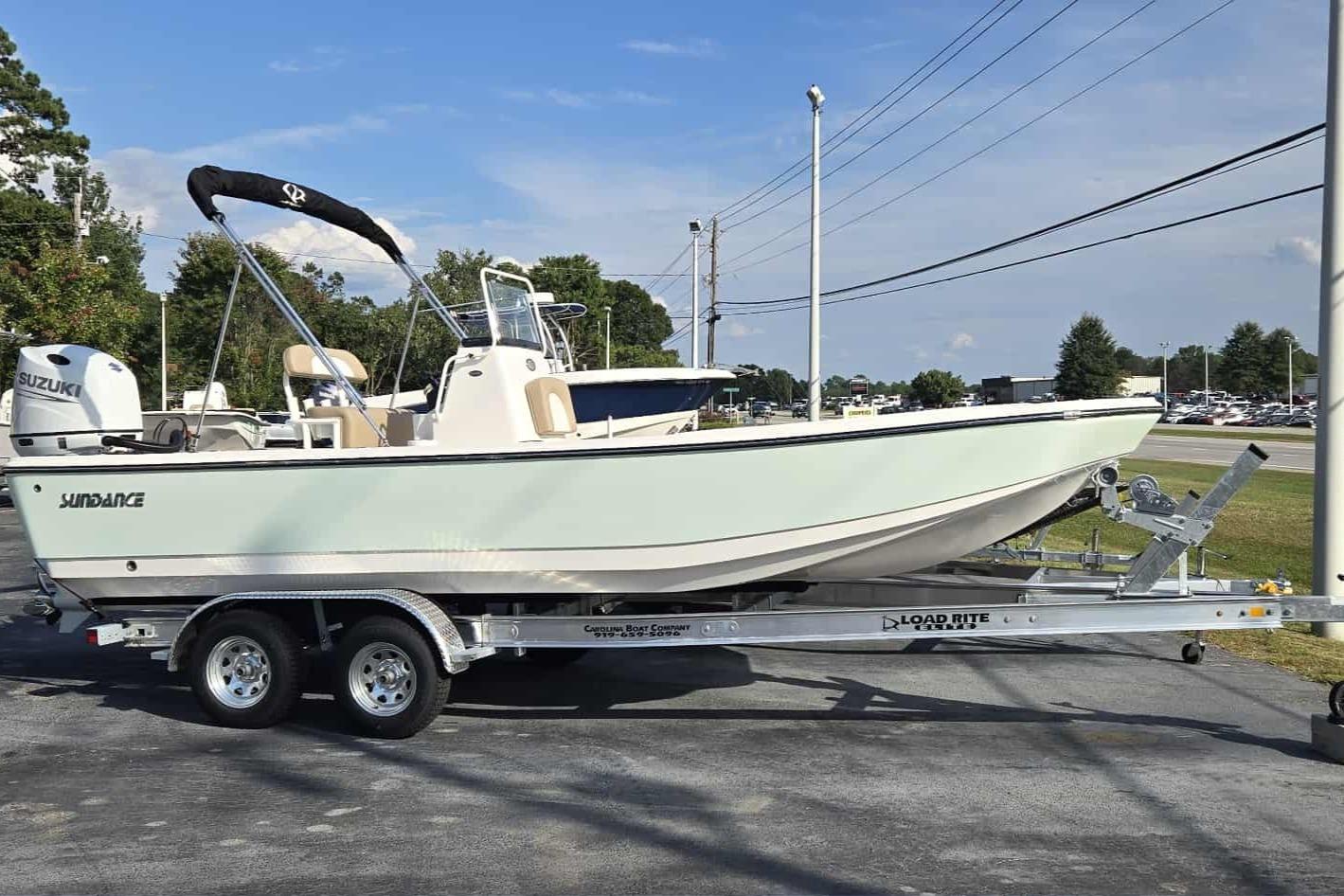 2026 Sundance DX22 boat on trailer, parked outdoors, featuring Suzuki engine.