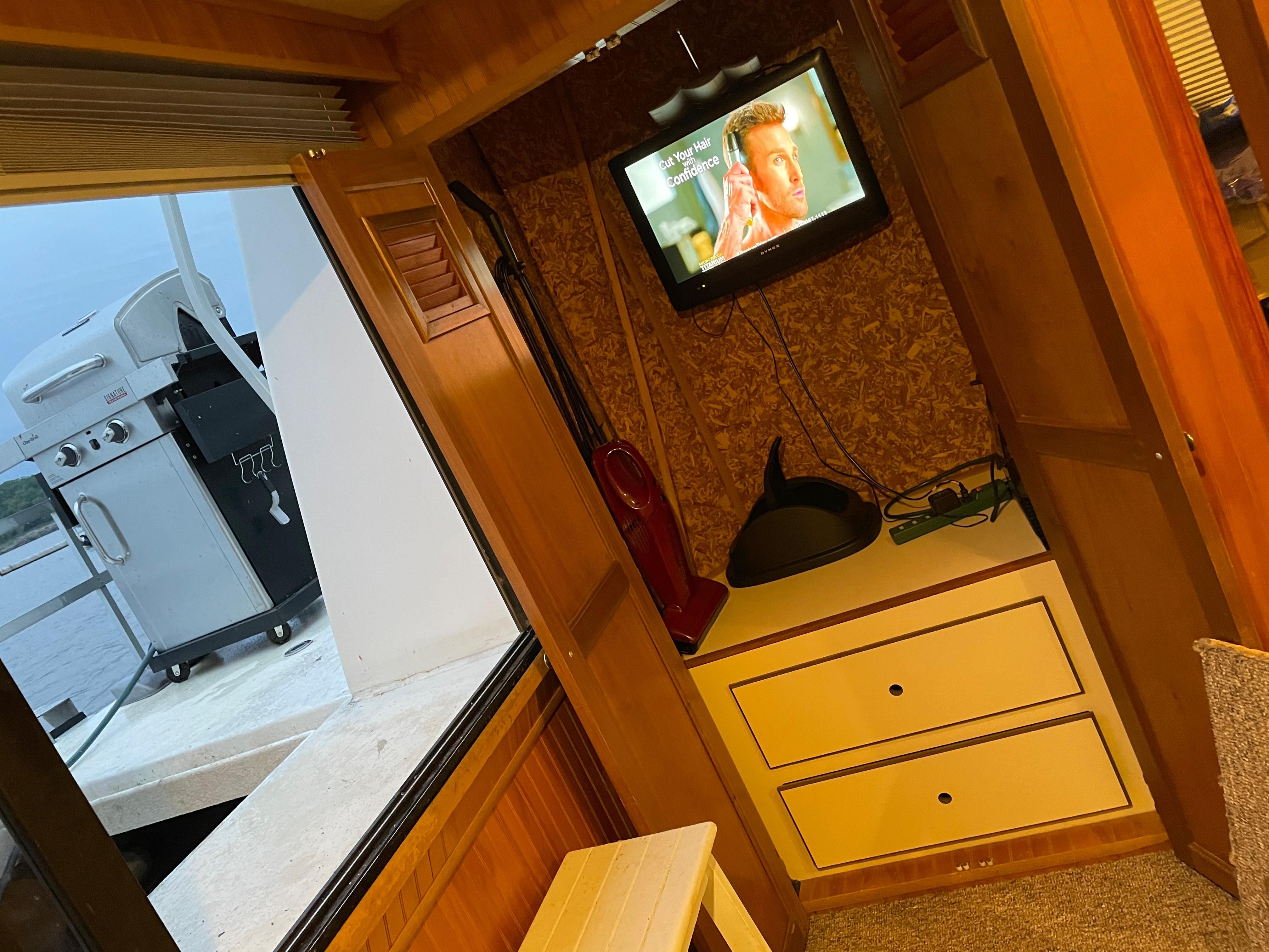 Interior of a boat with a TV and storage, view of a grill outside.