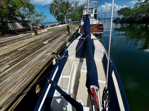 1968 Sailboat 24 docked by a wooden pier, surrounded by calm water and lush greenery.