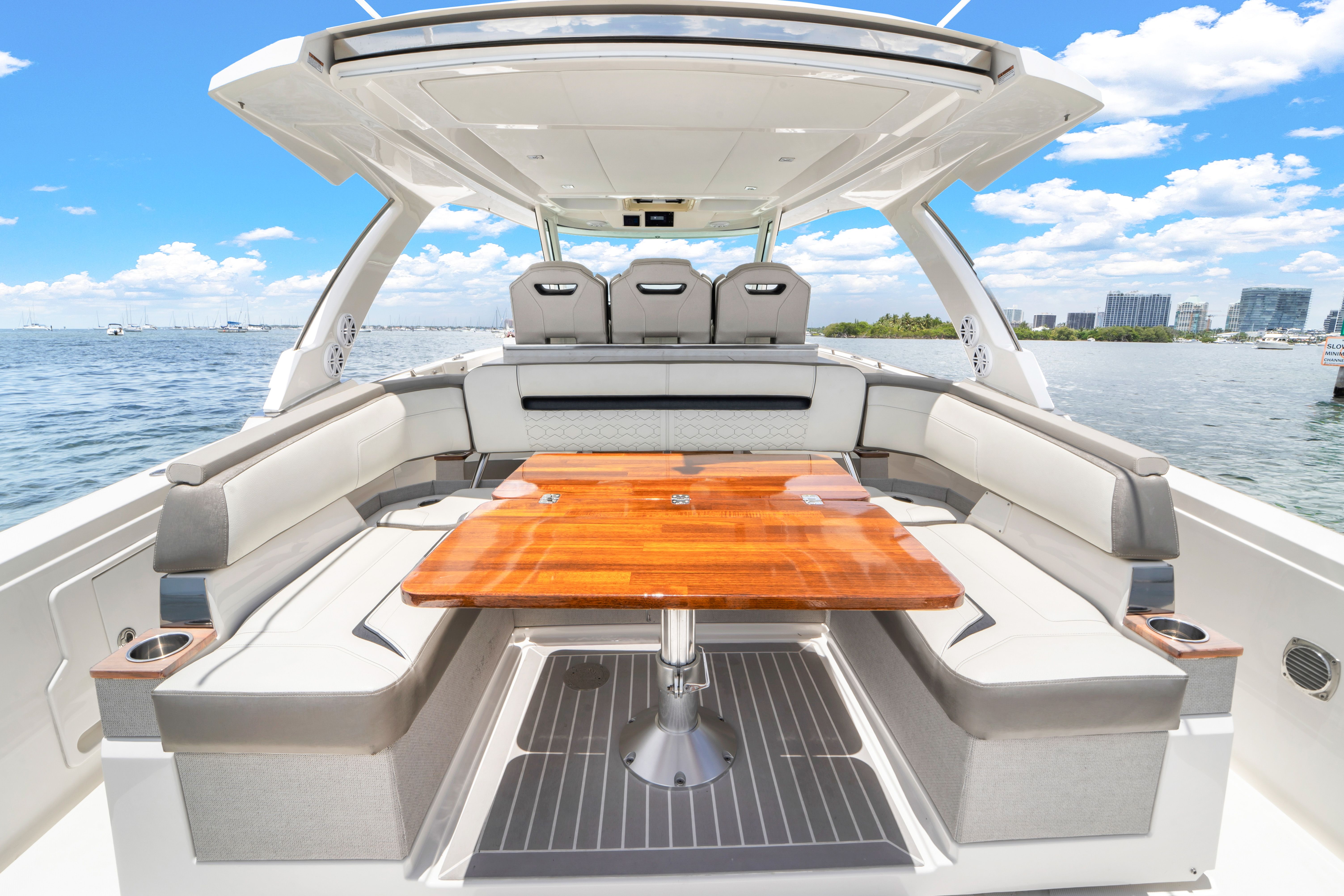 The image shows the stern of a 2023 Tiara Yachts 38 LS with a sleek wooden table and comfortable seating on the water.