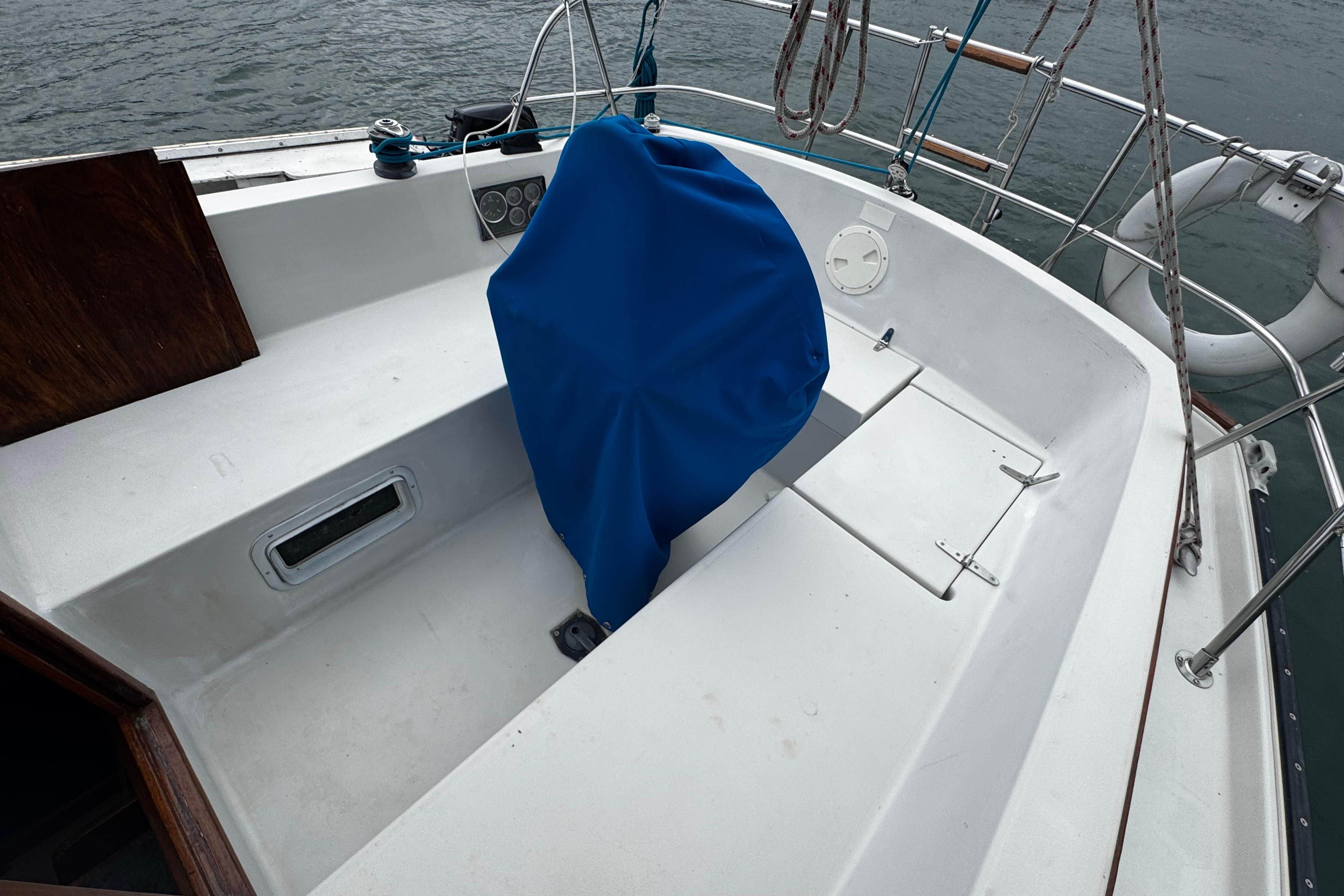 1984 Nonsuch 26 Classic sailboat cockpit with blue-covered wheel, docked on calm water.