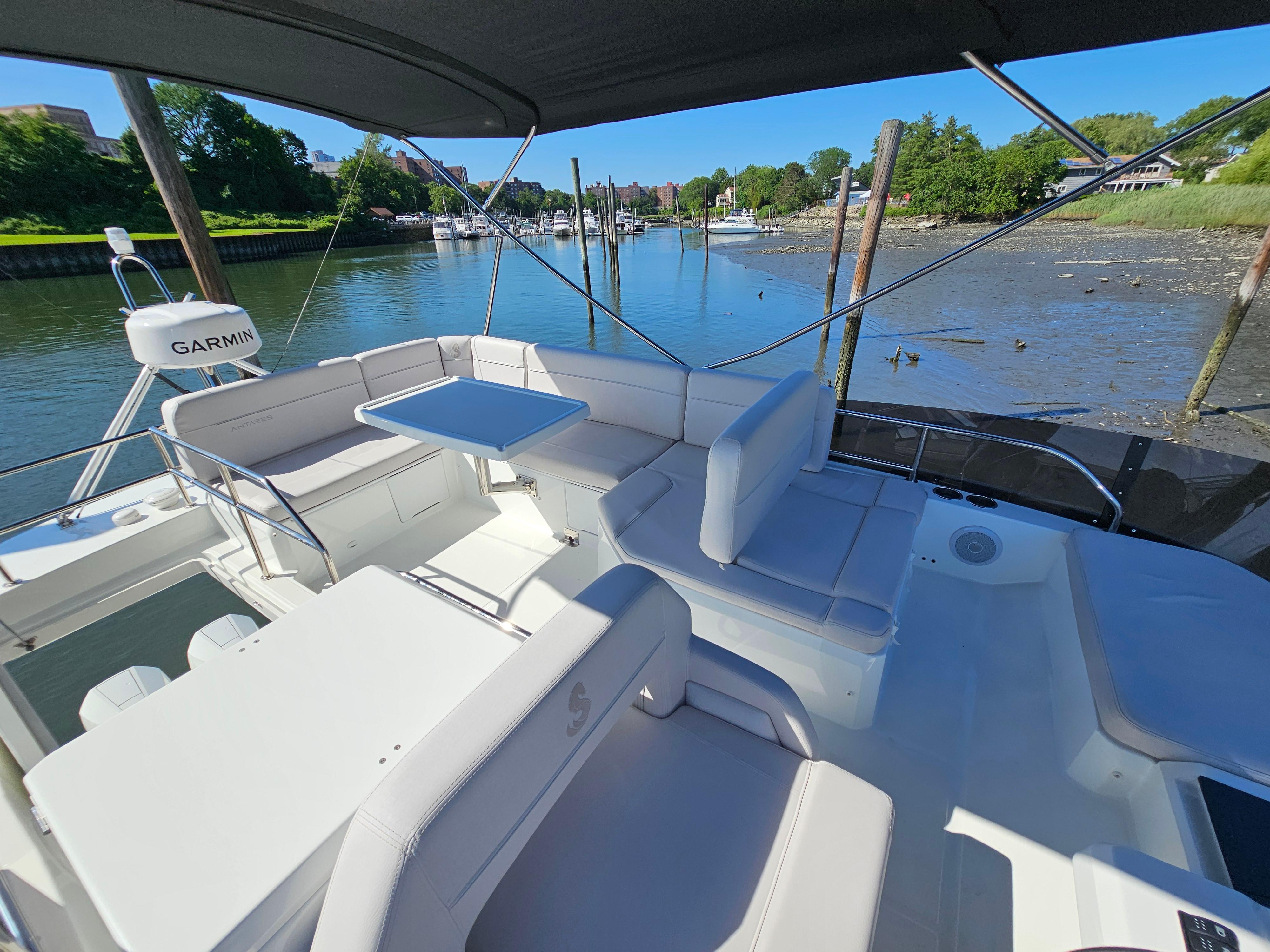 2024 Beneteau Antares 12 yacht interior with seating and table, docked by a scenic river.