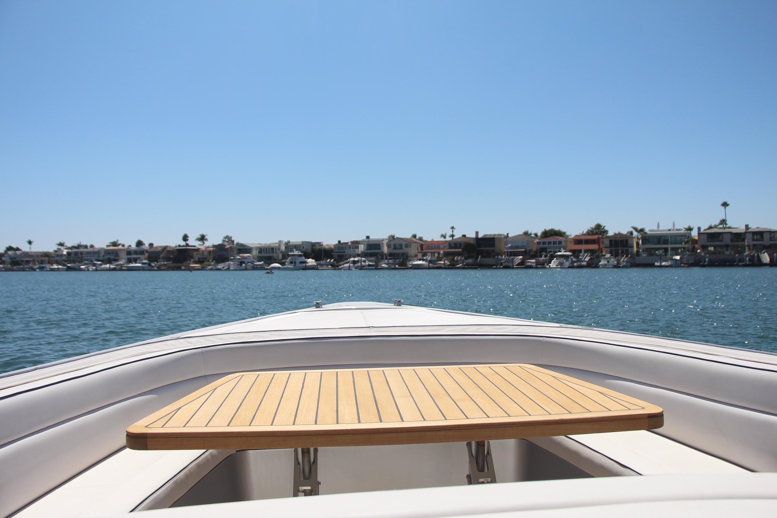 Bow view of 2017 Maori 50 boat with wooden table, coastal houses in background.