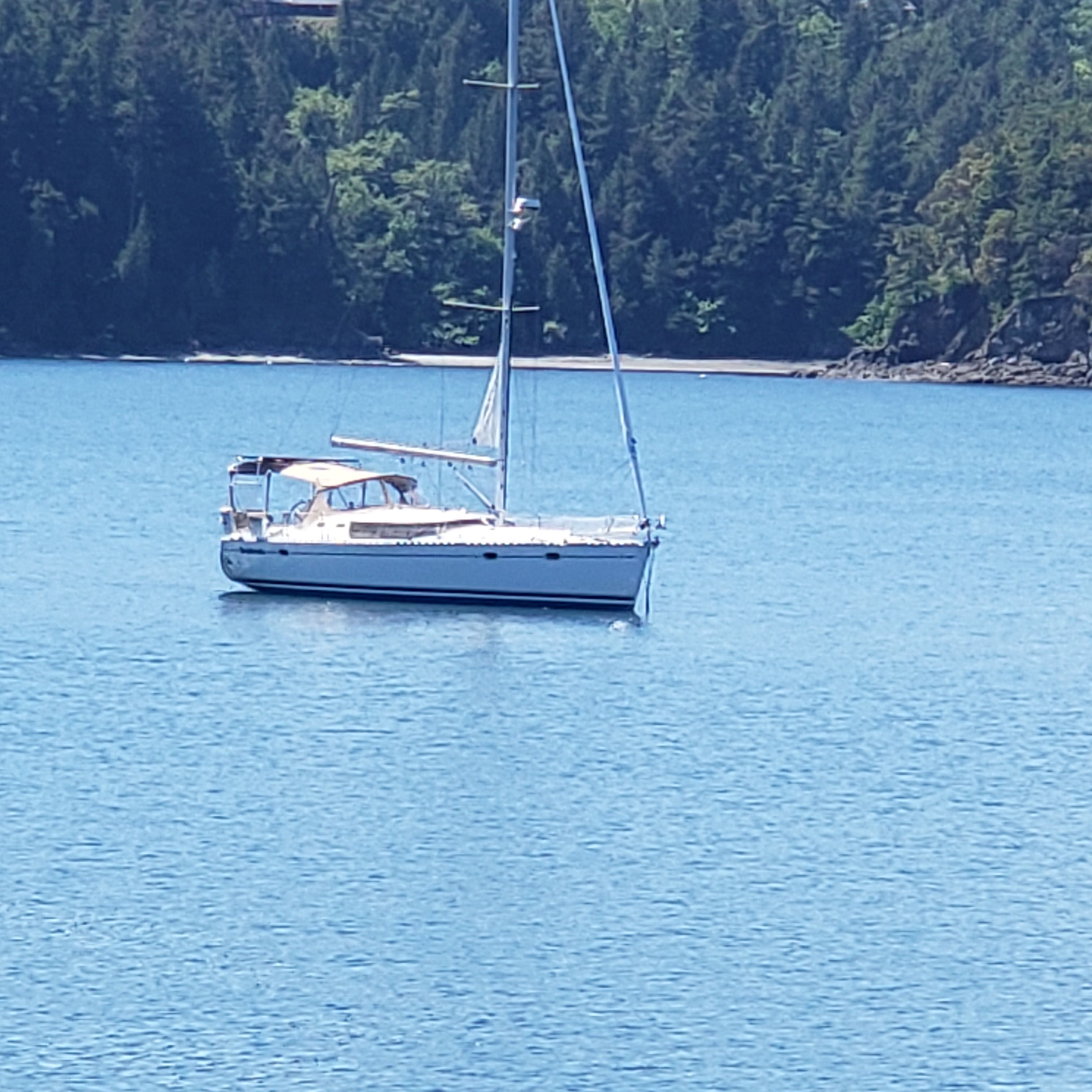 Sailboat on calm water near a wooded shoreline.
