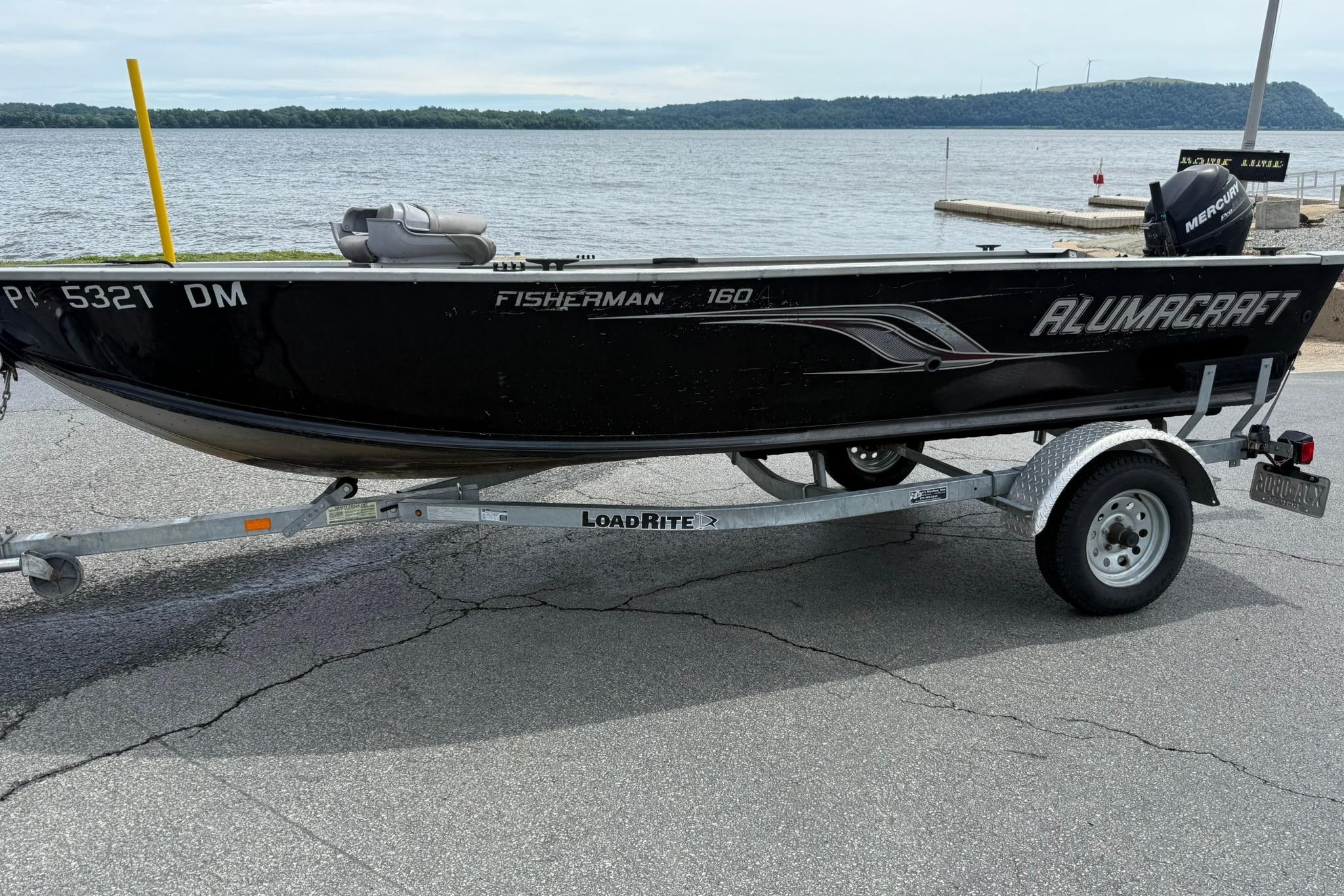 2013 Alumacraft Fisherman 160 Tiller boat on trailer by a lake.