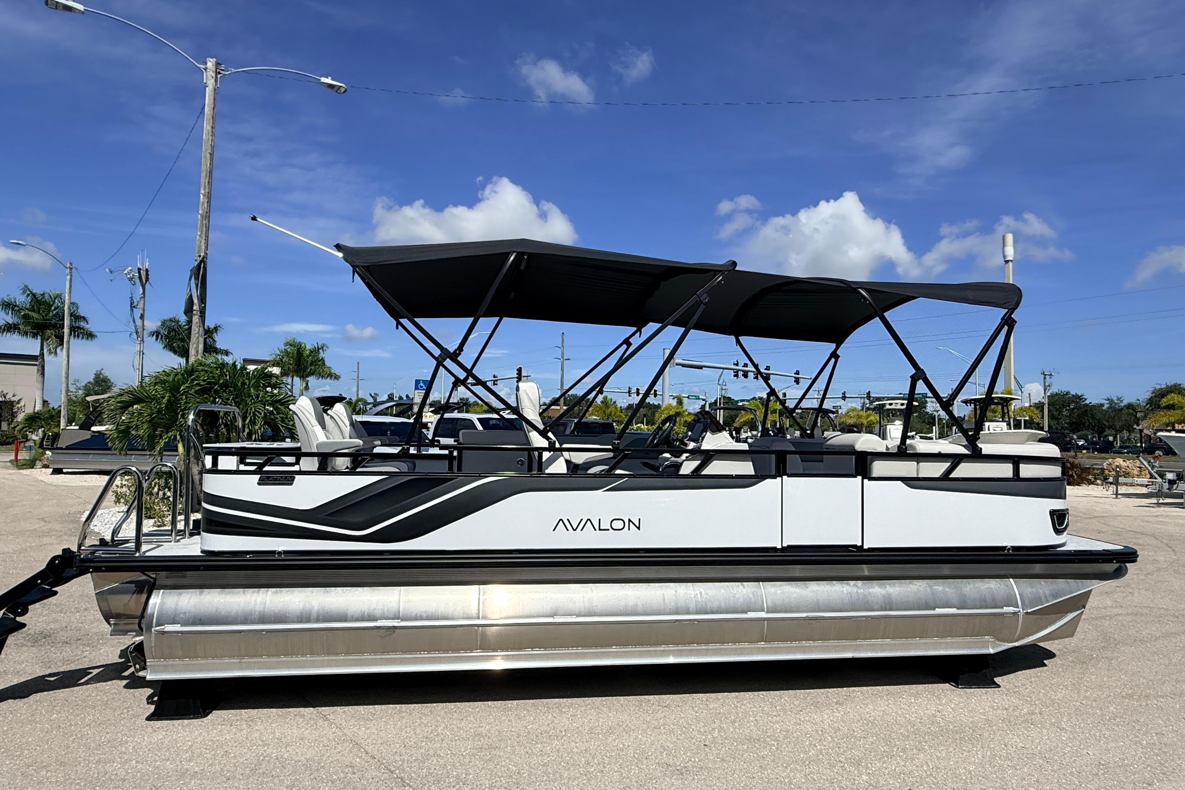 2026 Avalon 2385 Venture 85 Tri Toon boat with canopy, parked outdoors under blue sky.