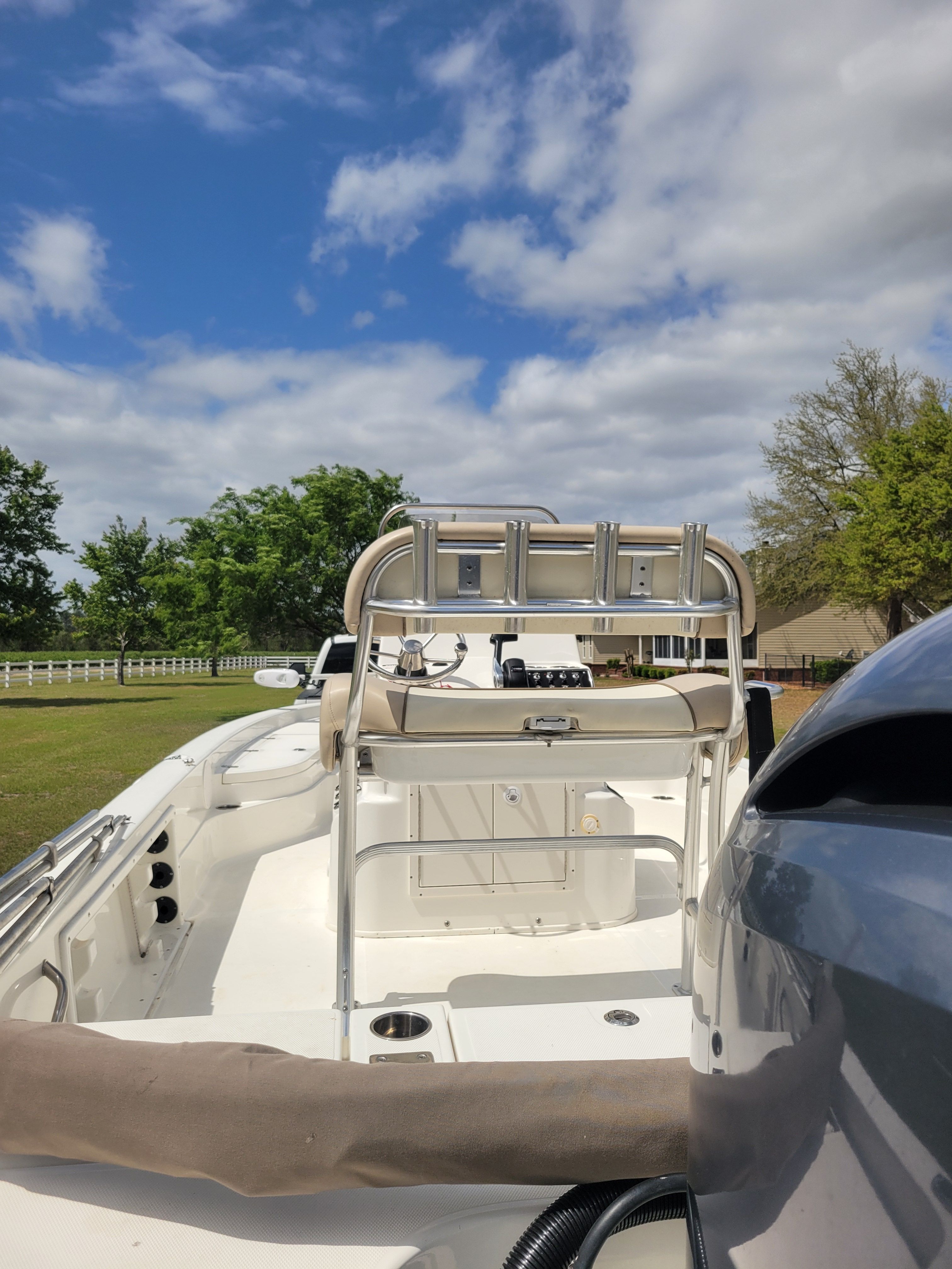 A white boat is on a trailer on grass under a cloudy sky.