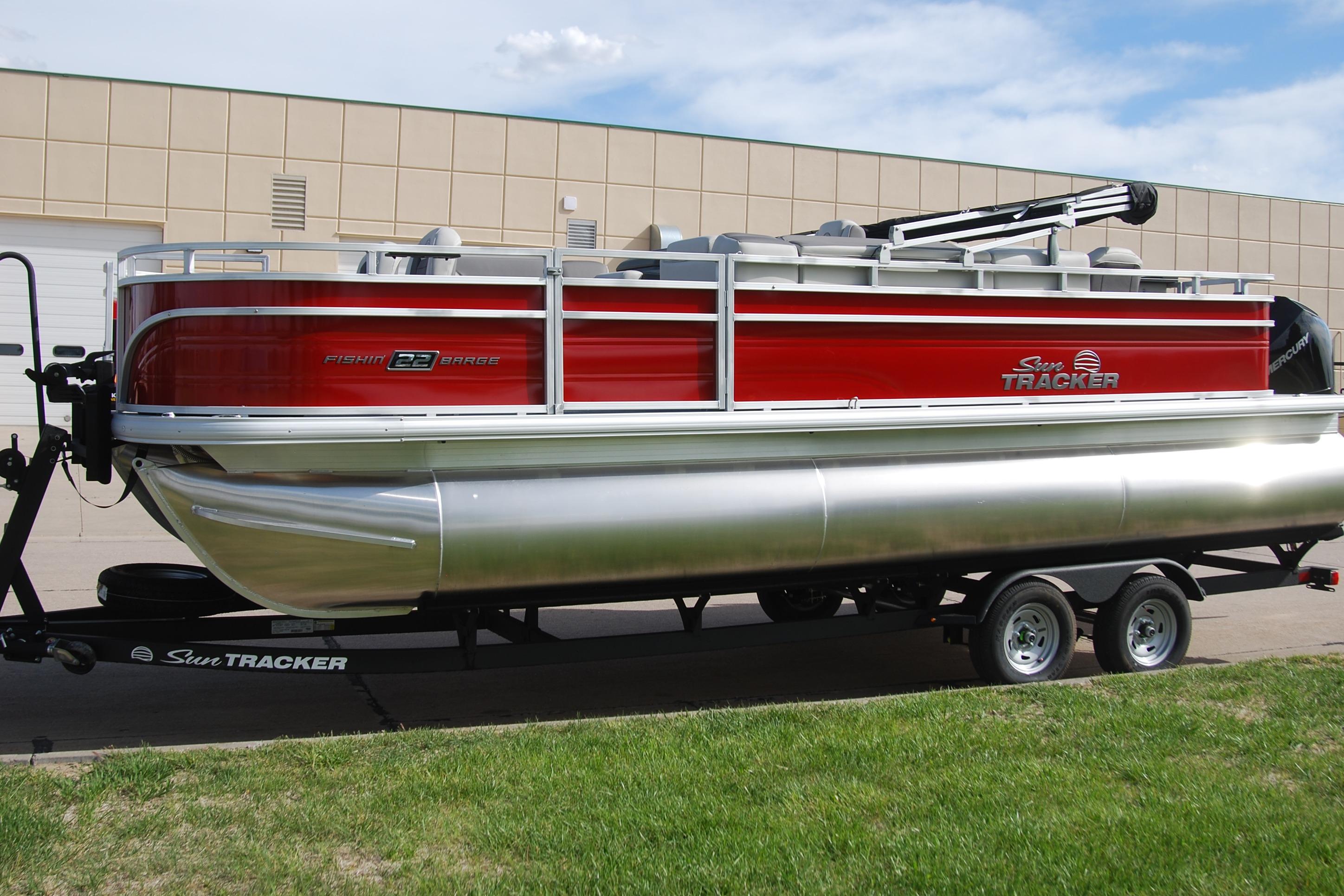 2026 Sun Tracker Fishin' Barge 22 XP3 pontoon boat on trailer, red and silver design.