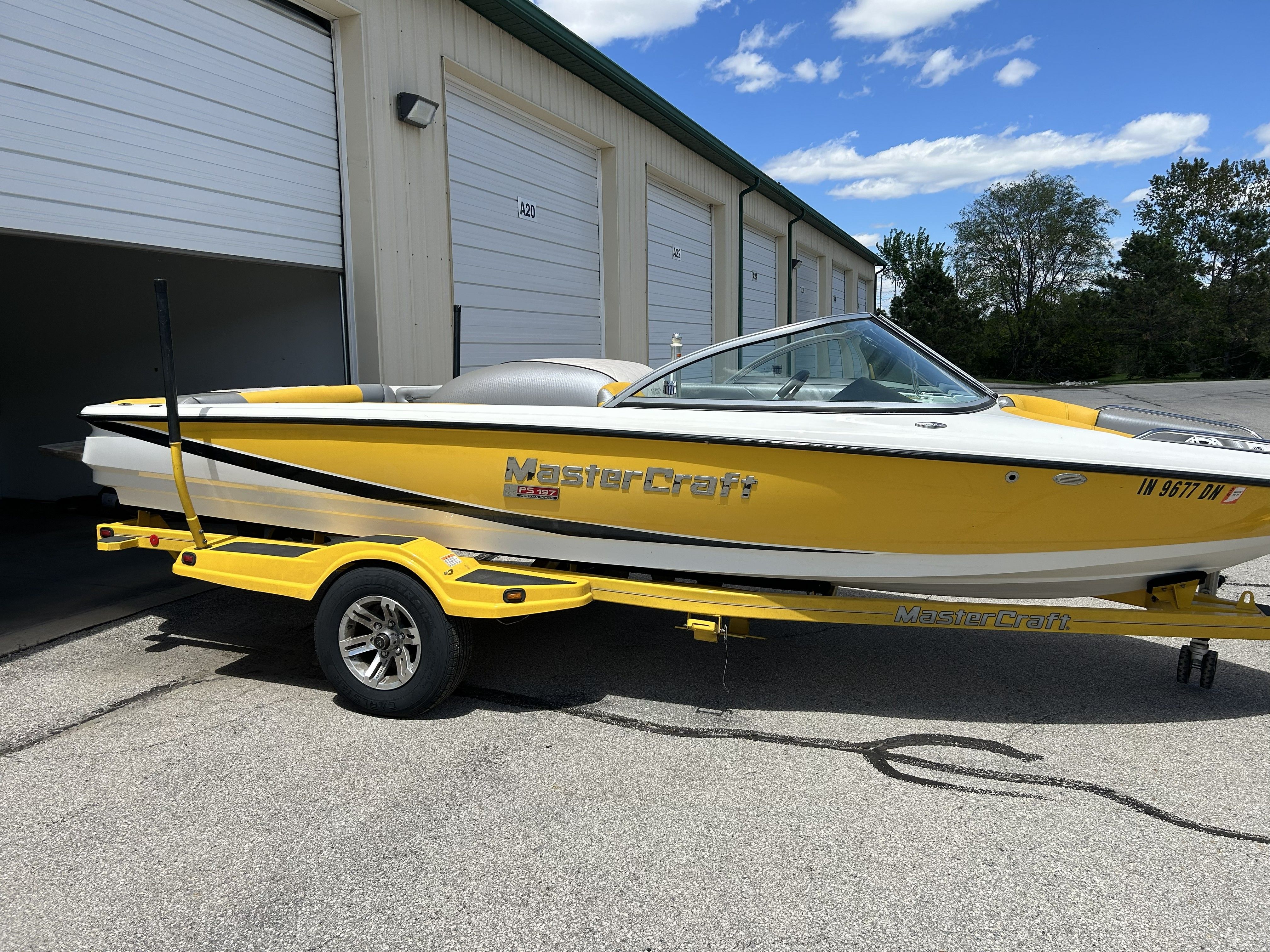 Yellow 2011 MasterCraft PS197 boat on trailer outside storage facility.