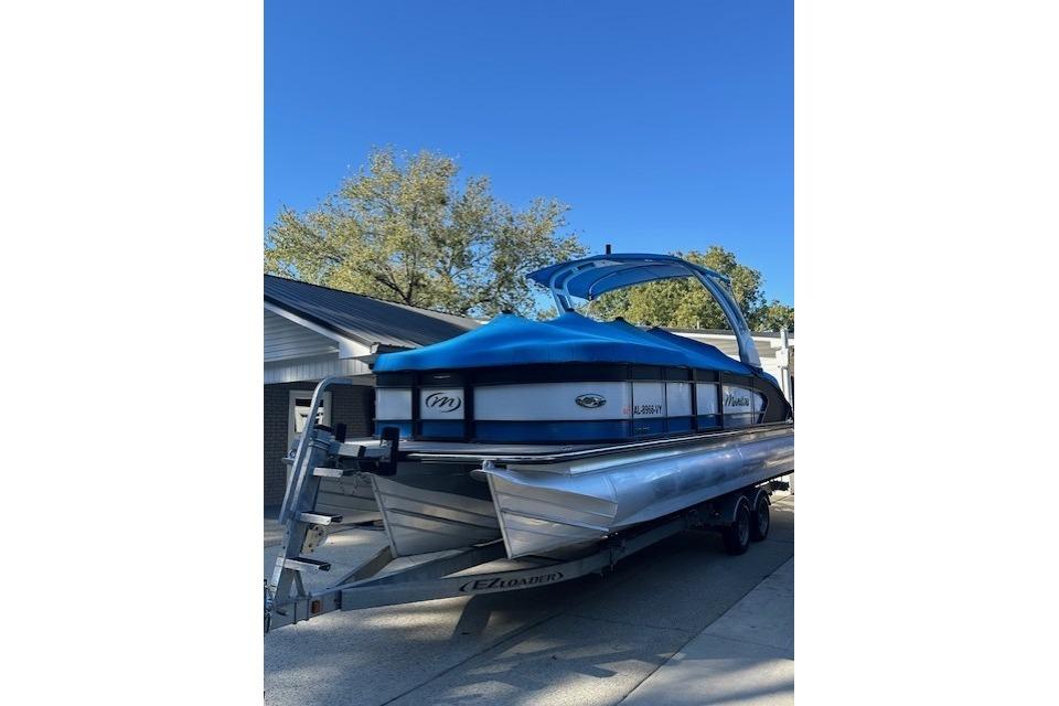 2020 Manitou 25 X-Plode RFW pontoon boat on trailer, blue cover, sunny day.