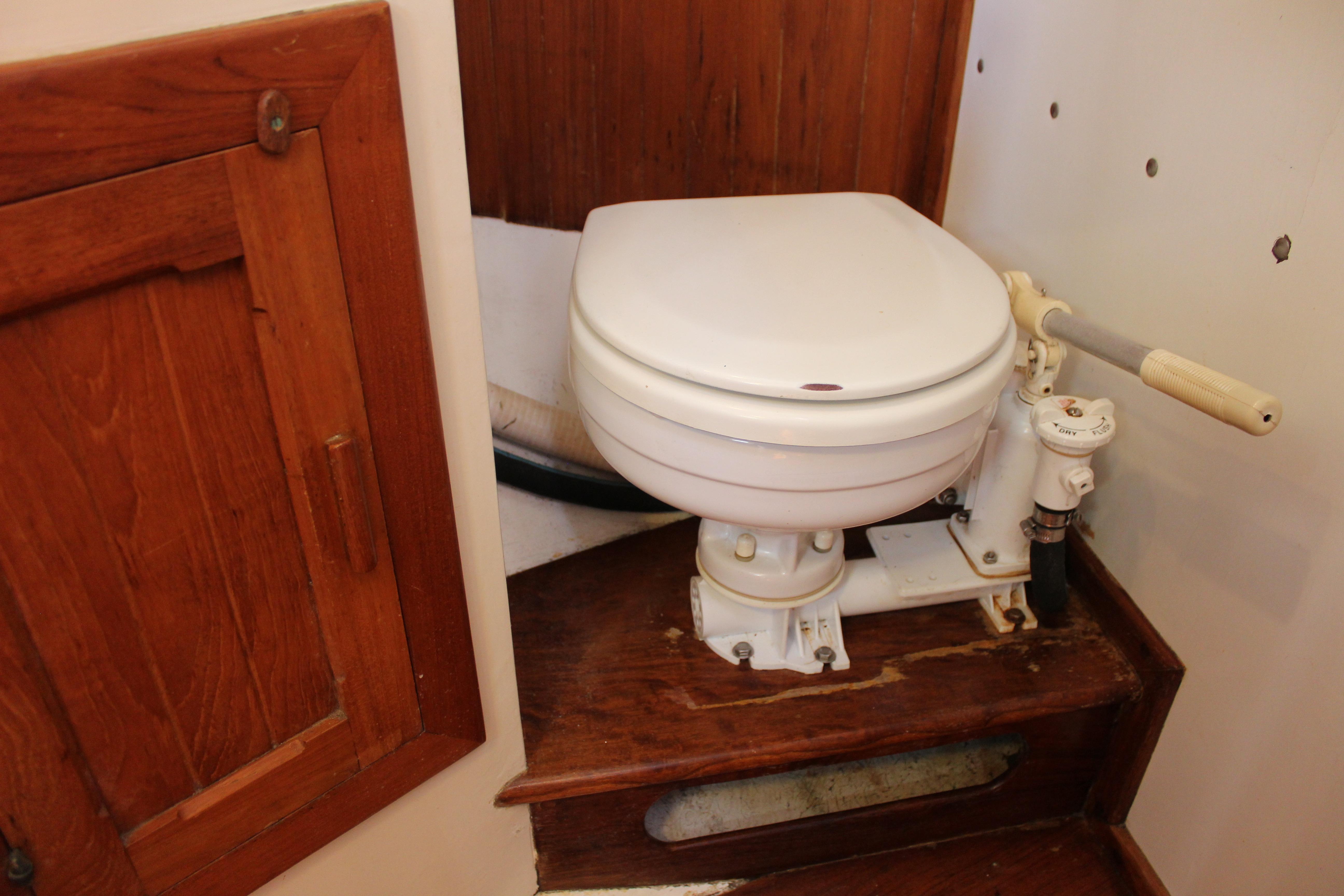 Marine toilet in a 1981 Kelly Peterson 46 sailboat, featuring wooden cabinetry.