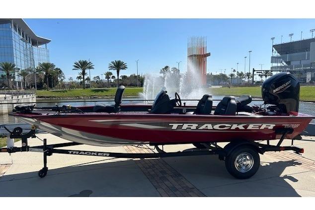2026 Tracker Pro Team 175 boat on trailer, parked near fountain and modern buildings.