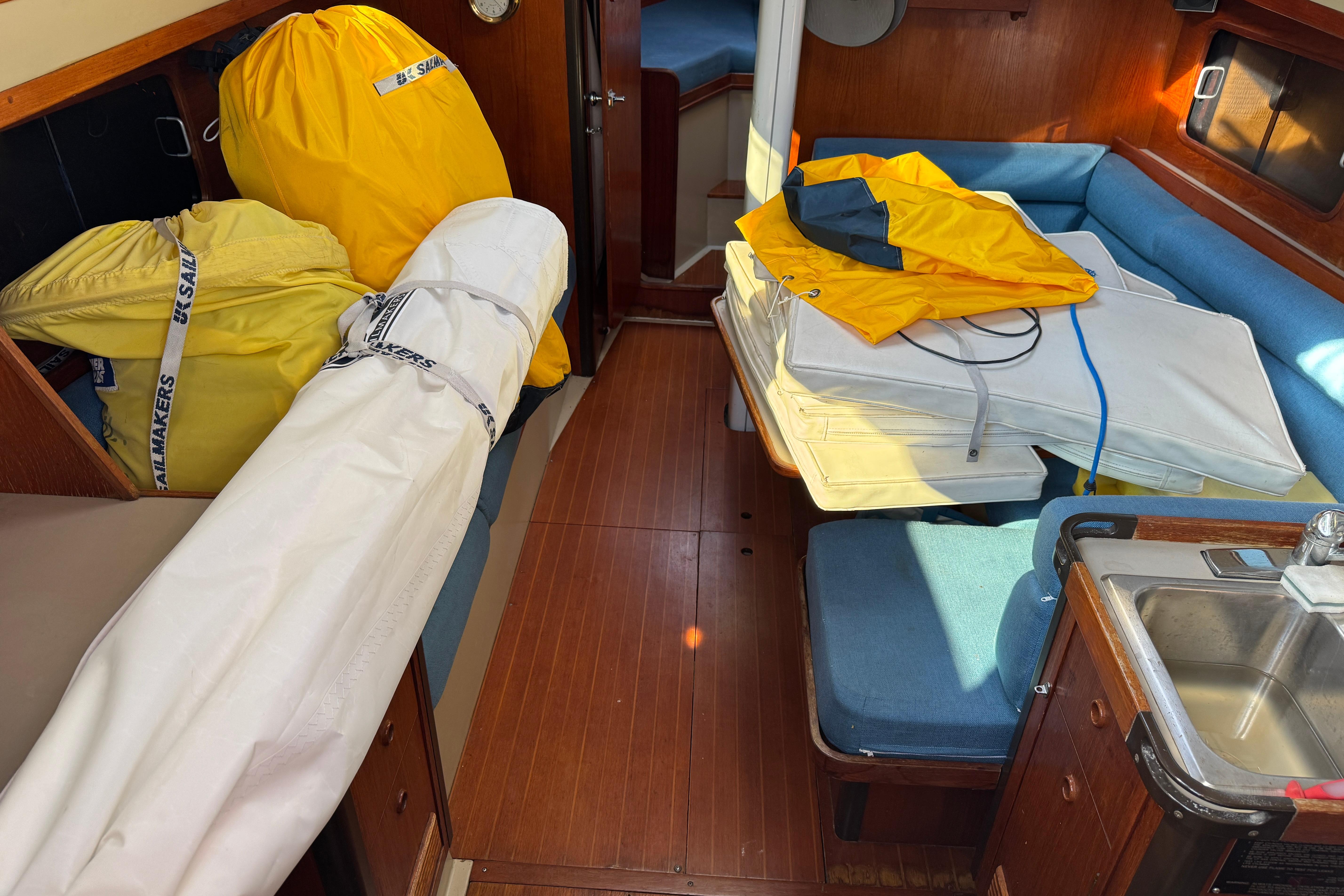 Interior of 1984 C&C Landfall sailboat with sails and cushions on blue seating.