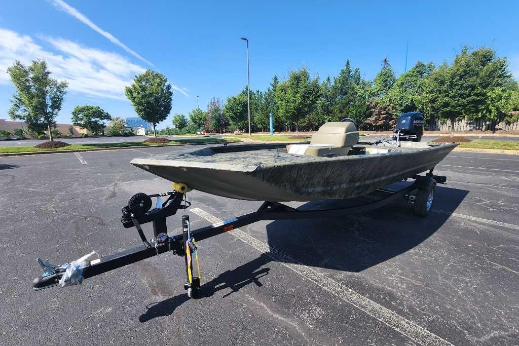 2026 Tracker Grizzly 1648 SC boat on trailer in parking lot, surrounded by trees.