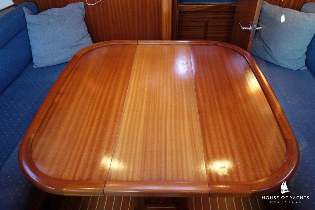 Interior of 2003 Bavaria 32 yacht with polished wooden table and blue cushioned seating.