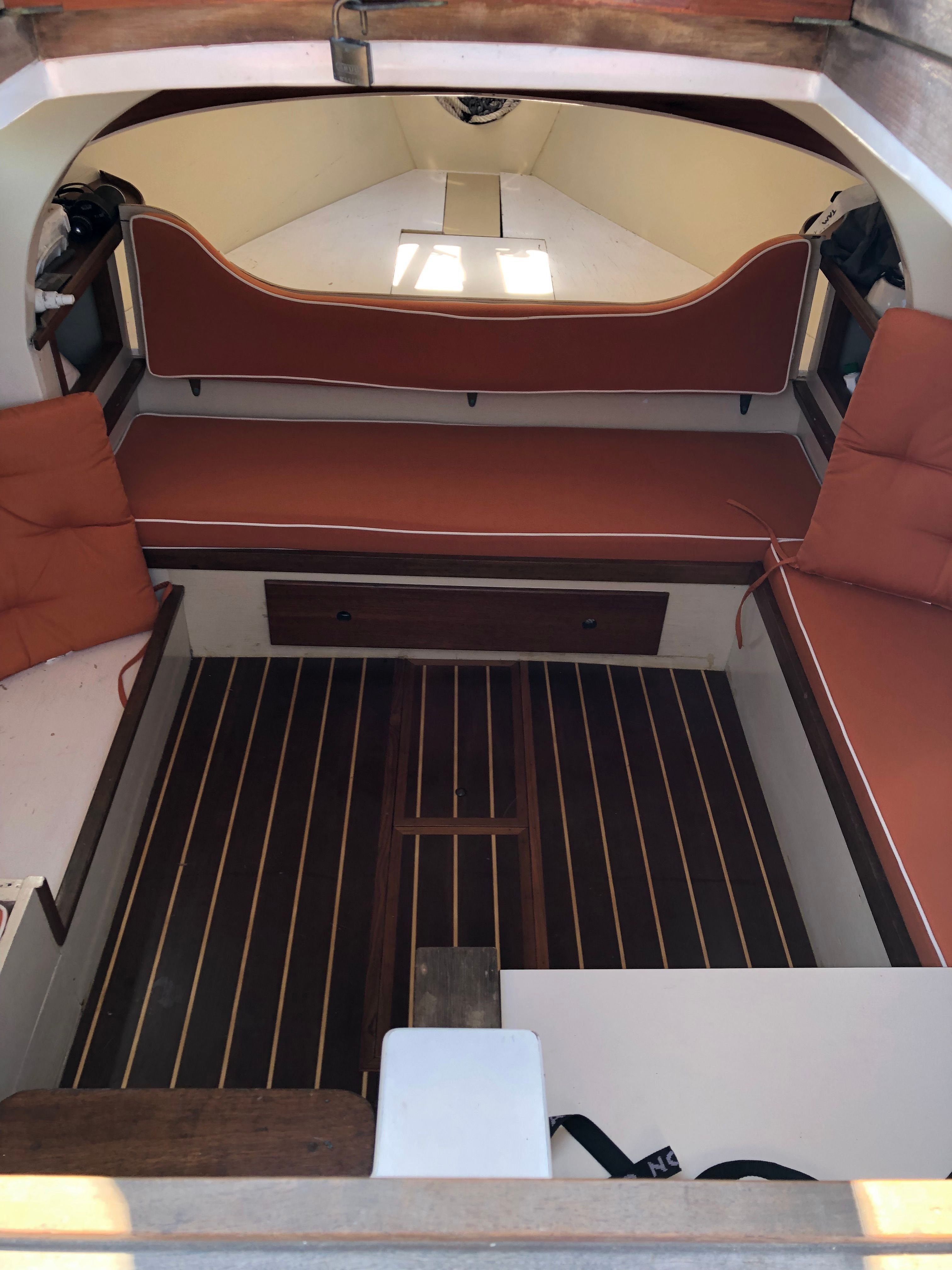 Interior of a 1973 Talman Yacht Menemsha-24 with wooden flooring and red cushions.