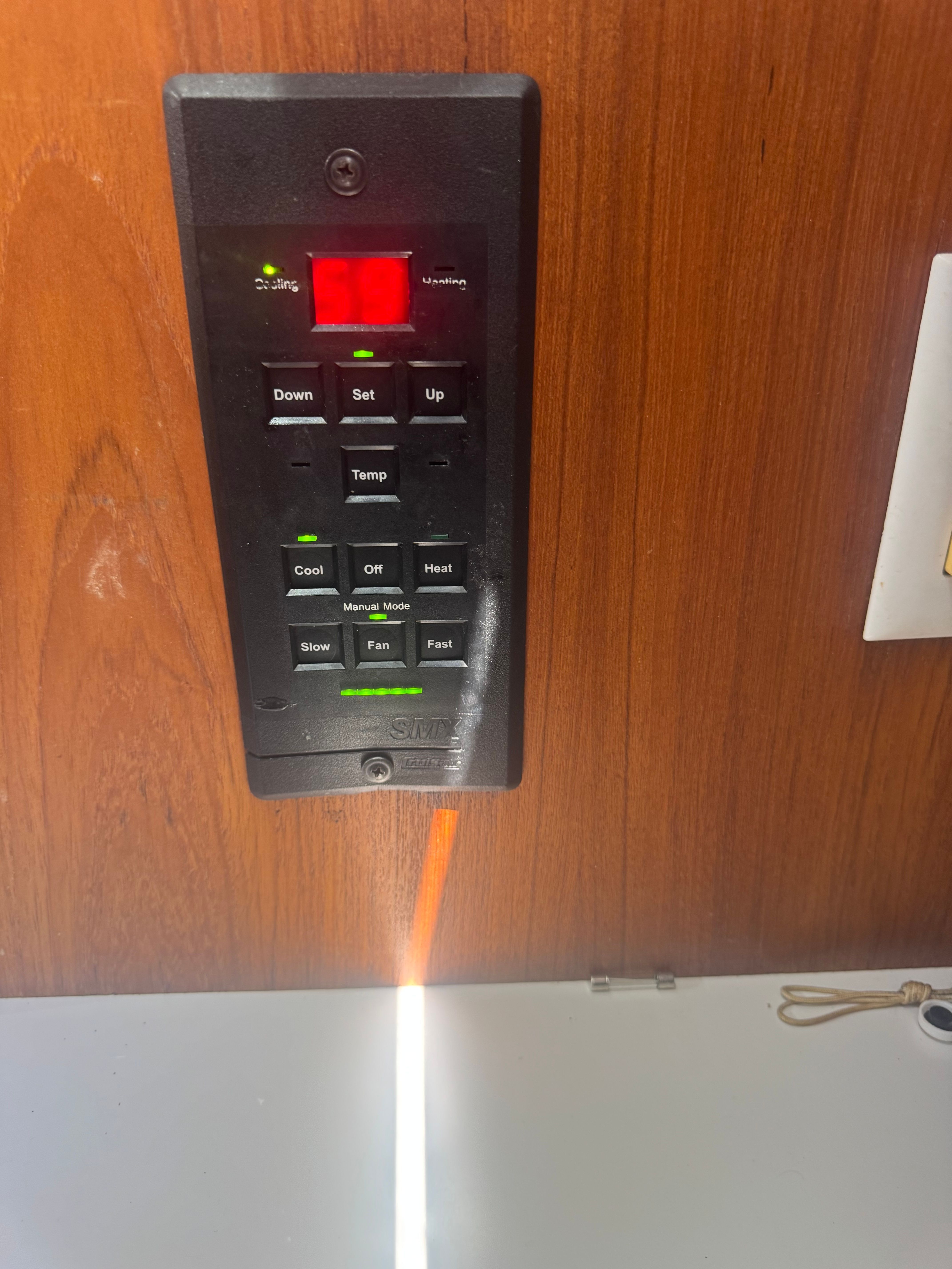 A control panel with buttons for temperature and fan speed is mounted on a wooden wall.