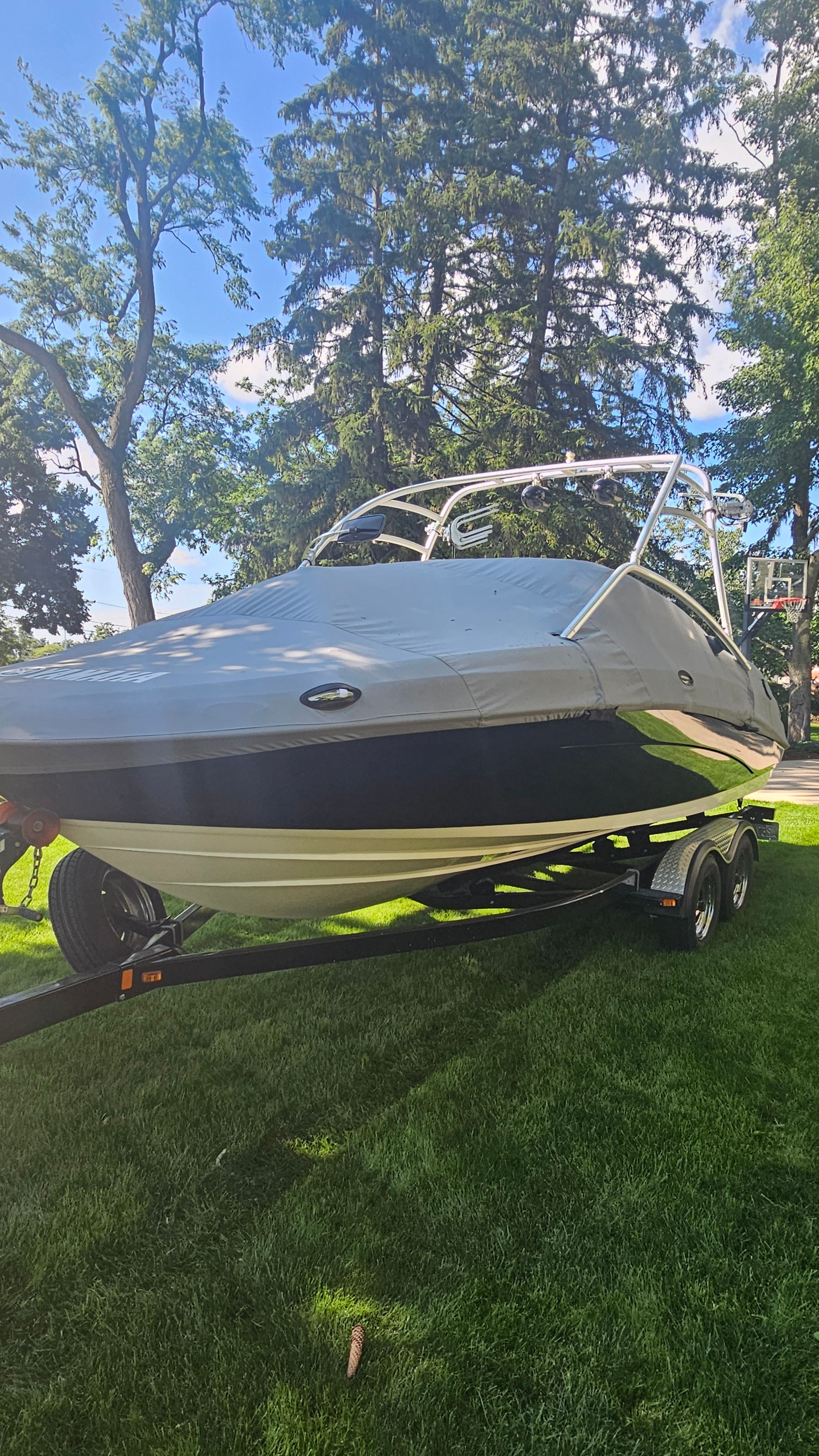 A 2010 Yamaha AR210 boat on a trailer, surrounded by trees and grass.