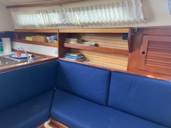 Interior of 1989 Catalina 30 sailboat with blue seating and wooden shelves.