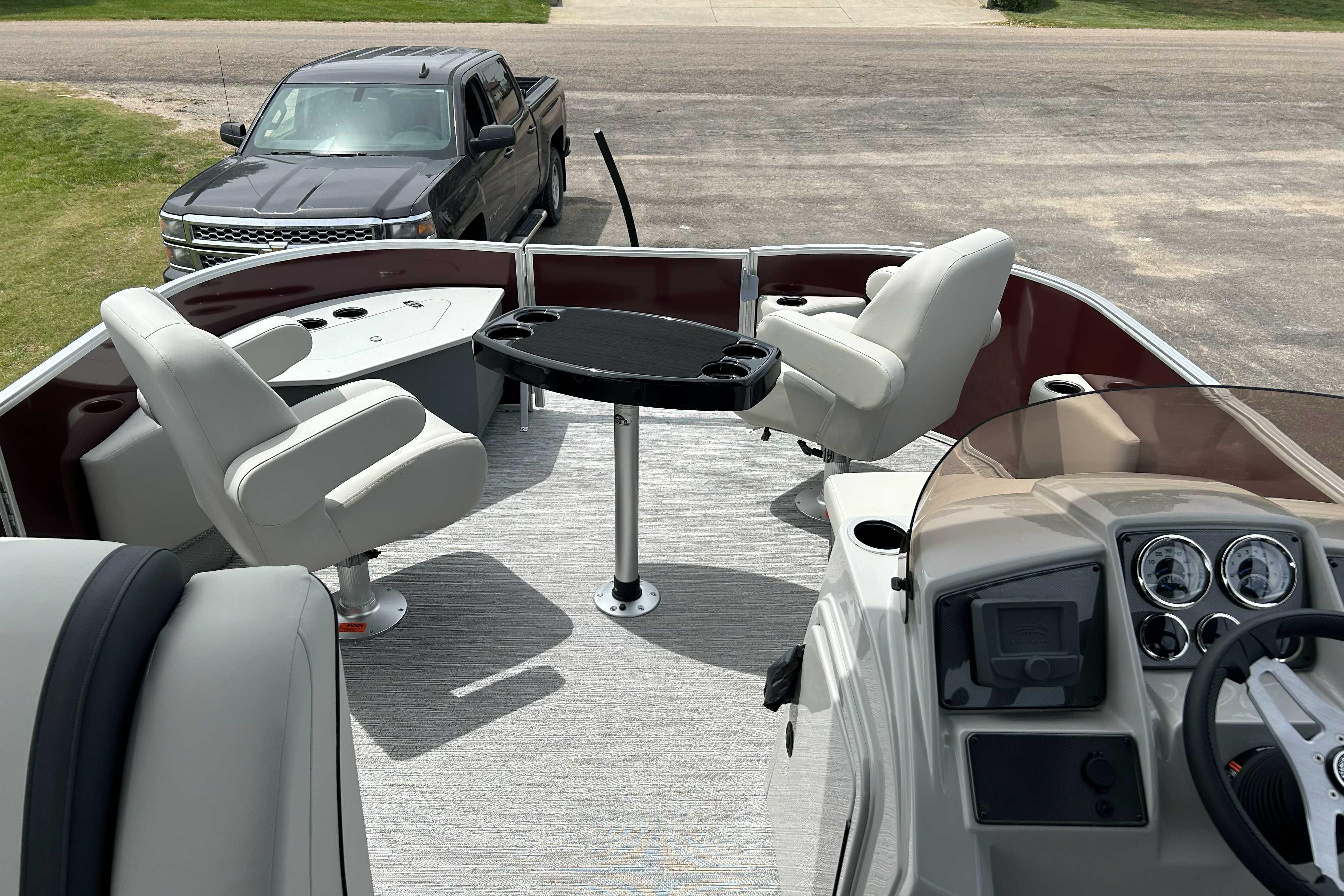 2026 Starcraft EX 20 F pontoon boat interior with seating and table, parked truck nearby.