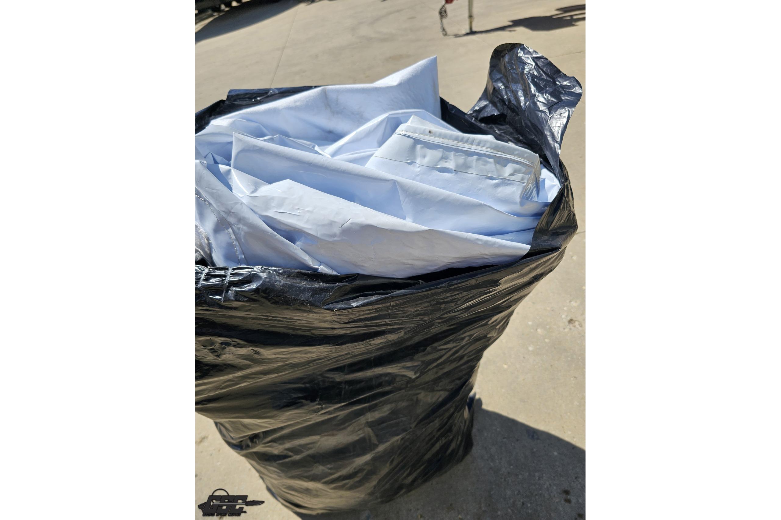 Black trash bag filled with folded white covers, outdoors on pavement.