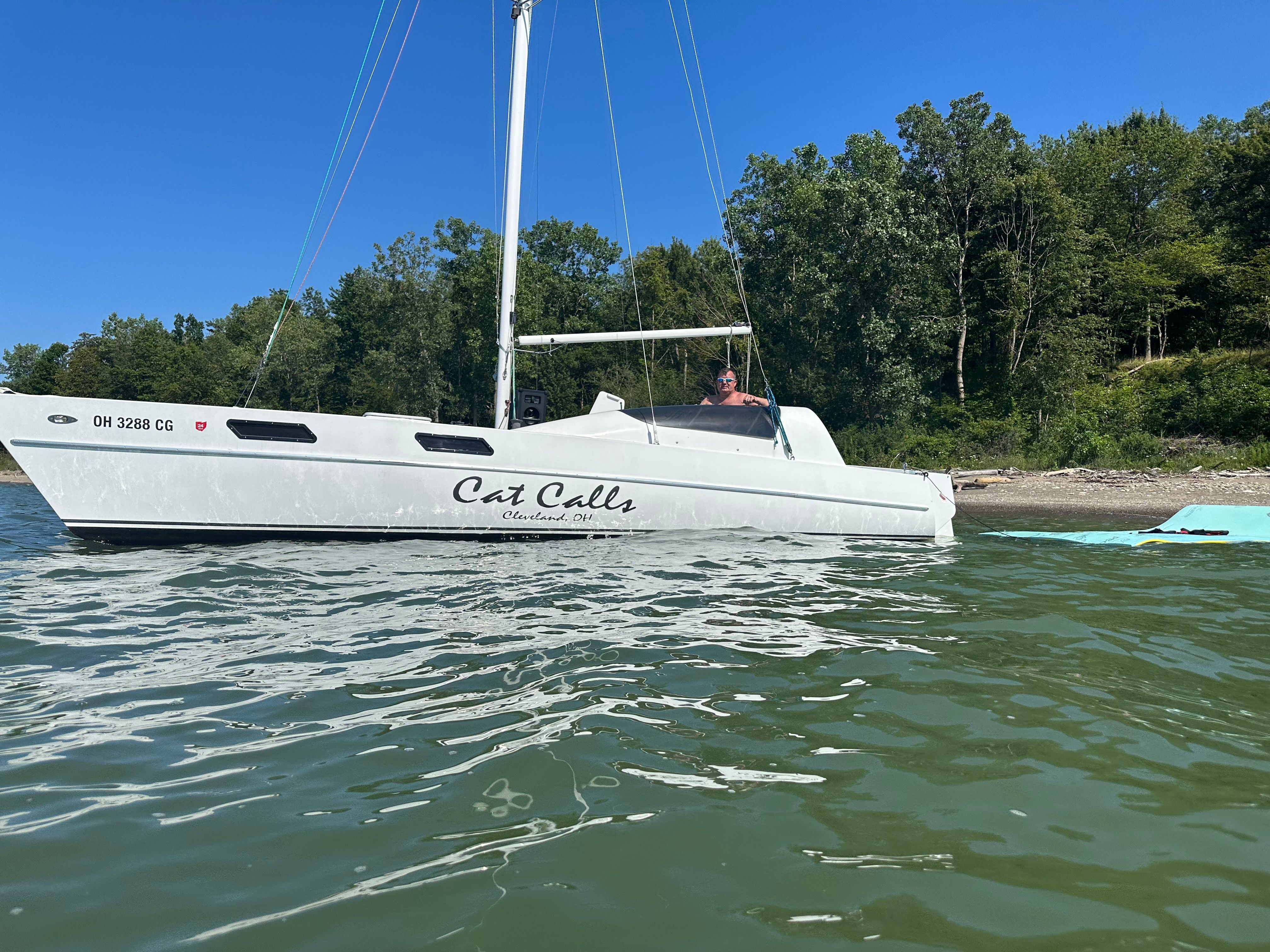 A white catamaran named "Cat Calls" sails on calm water, surrounded by trees.