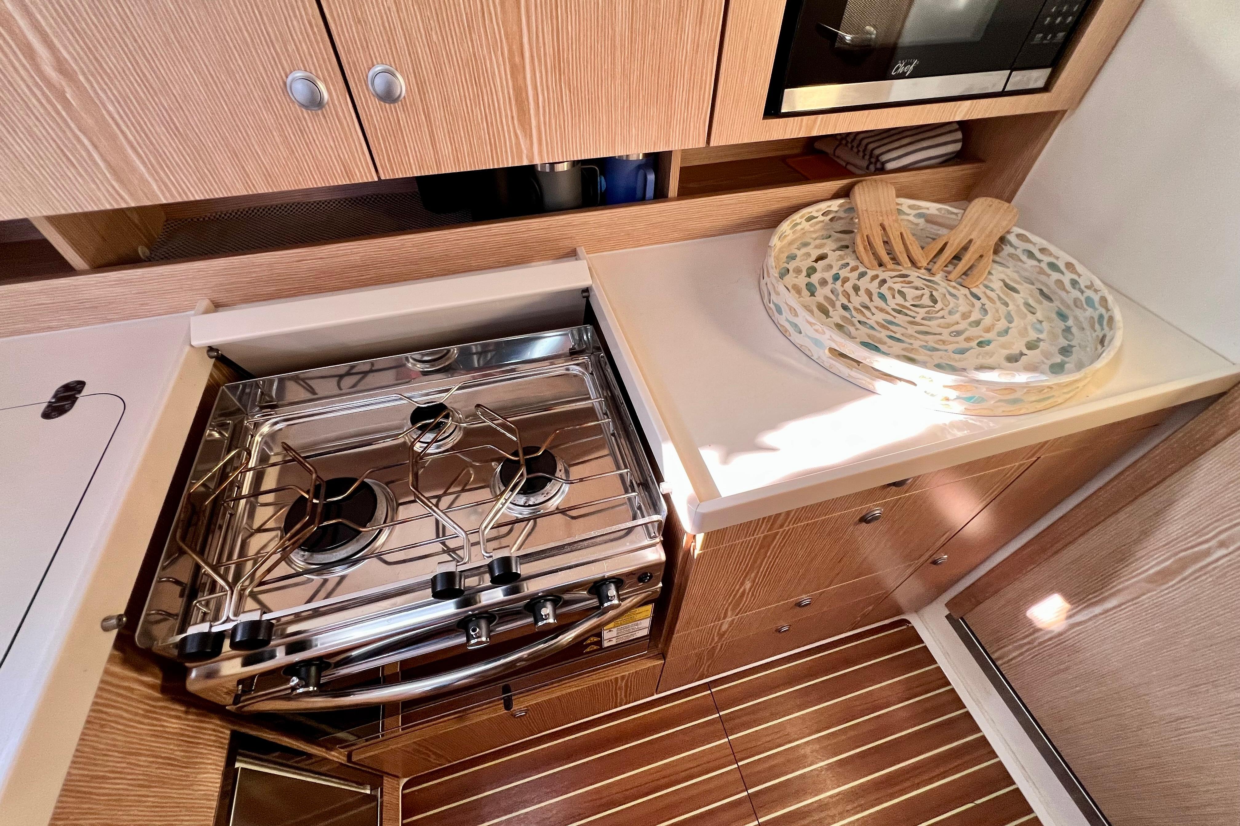 Modern kitchen in 2016 Hanse 455 yacht with stove, microwave, and wooden cabinetry.