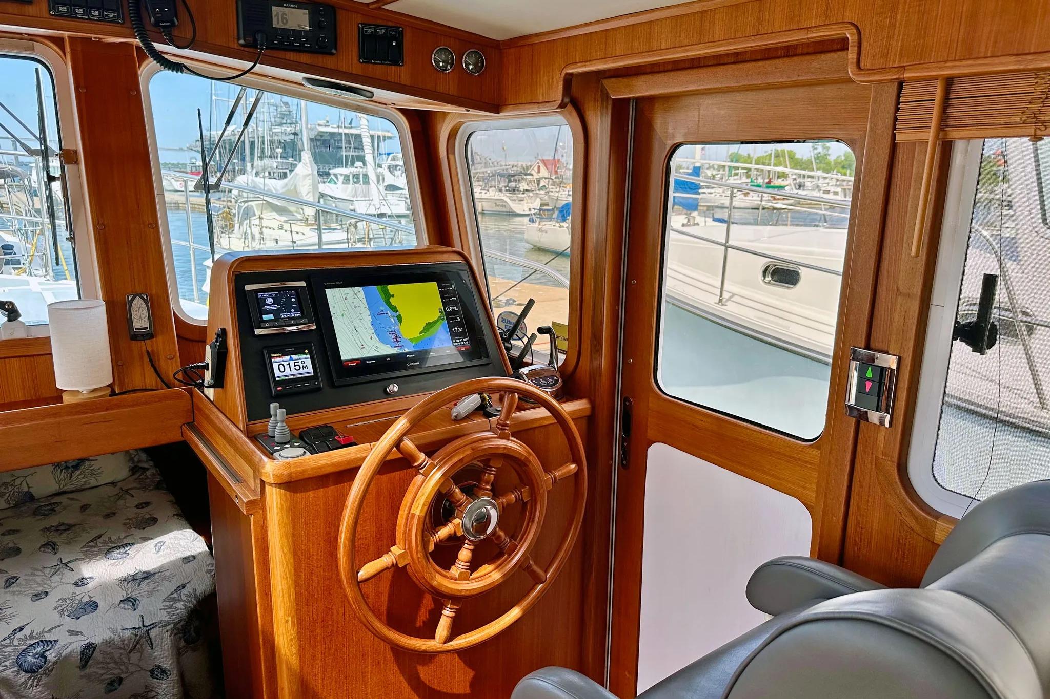 Pilothouse interior of 2016 Helmsman Trawlers 38, featuring navigation equipment and wooden steering wheel.