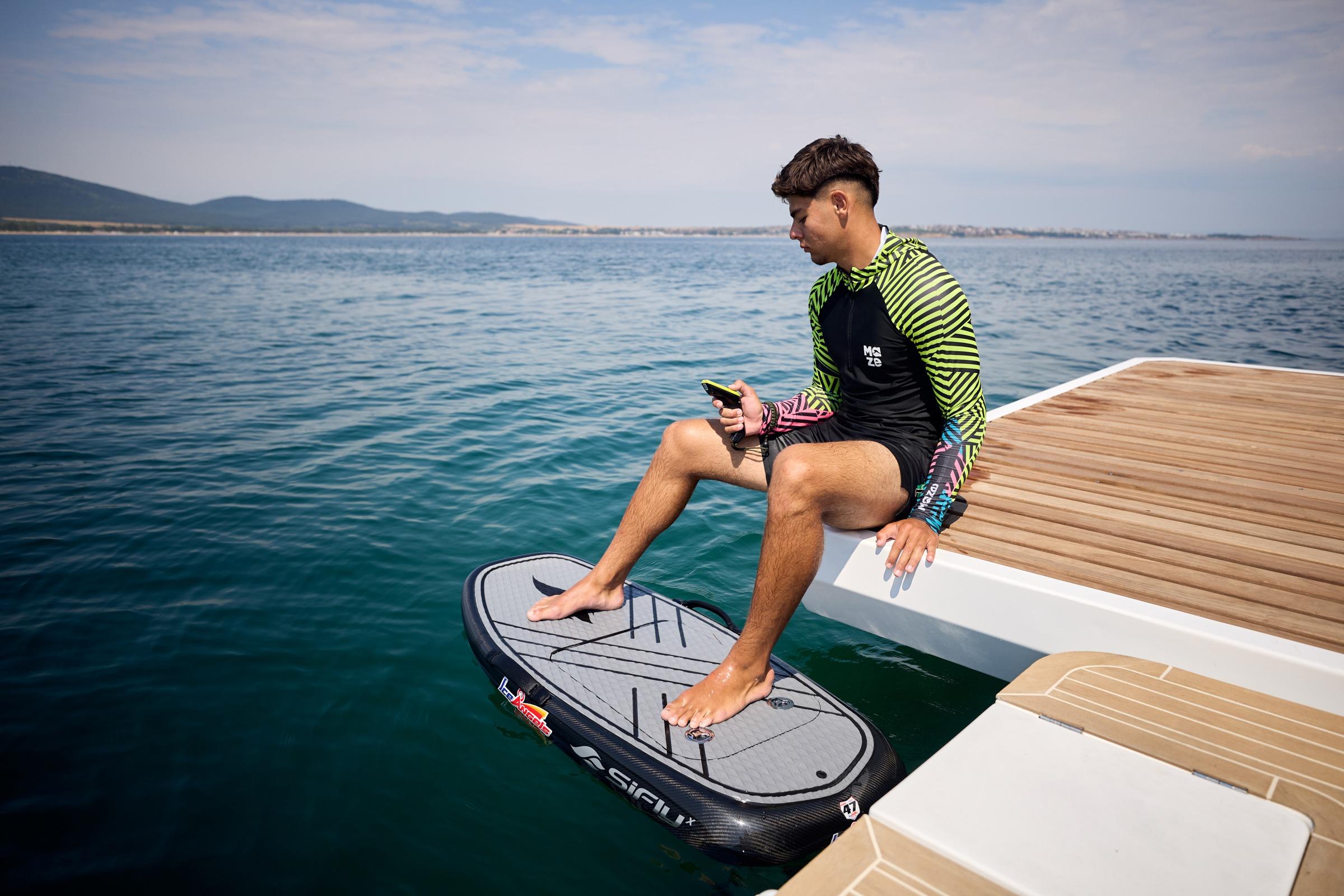 Man sitting on a Custom Omaya 50 Power Catamaran, holding a phone, near a jetboard.