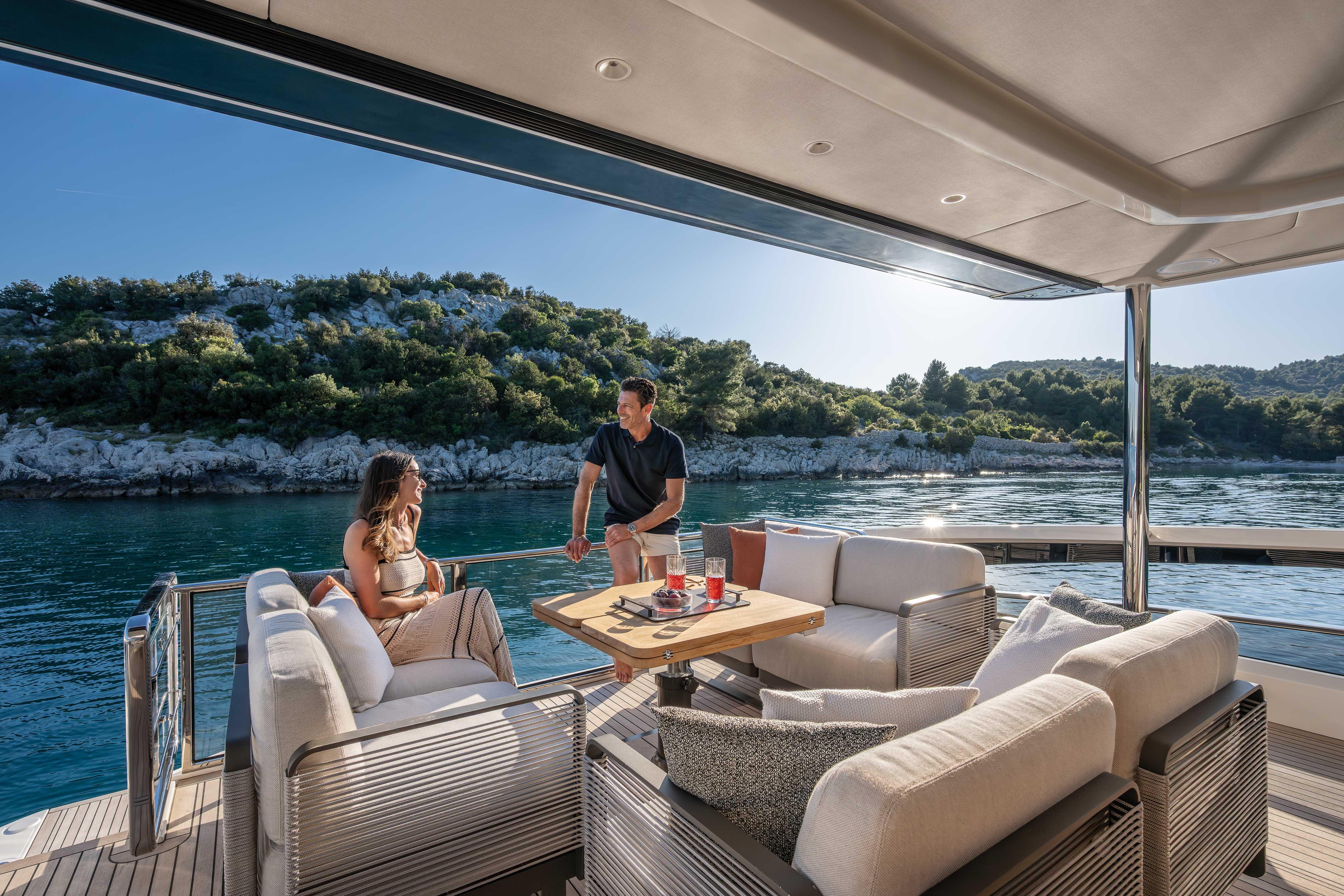 Two people relax on a luxurious boat overlooking a wooded coastline.