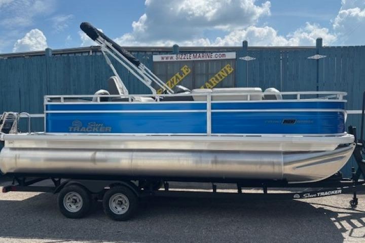2026 Sun Tracker Fishin' Barge 20 DLX pontoon boat on trailer, blue and silver design.