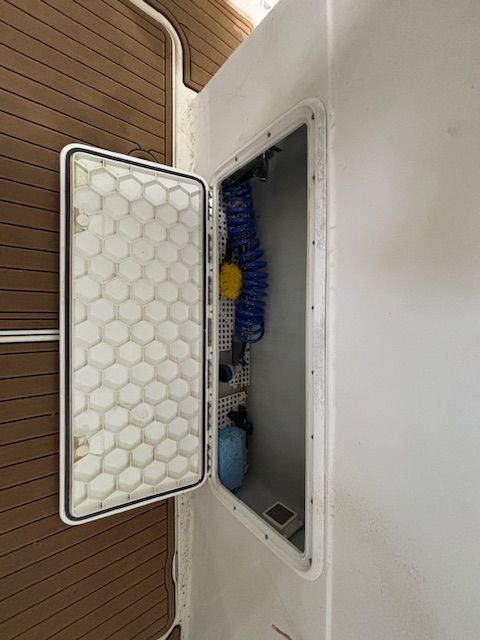 An open storage compartment on a boat with cleaning supplies and a blue hose.
