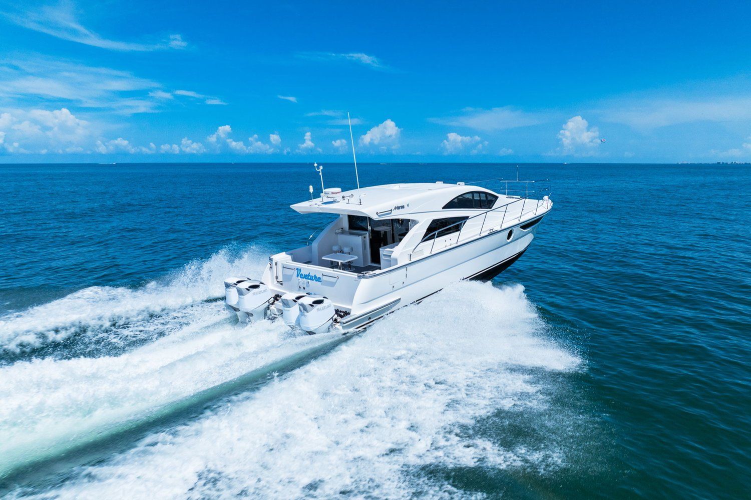 A white catamaran speeds across the blue sea, with a clear sky in the background.