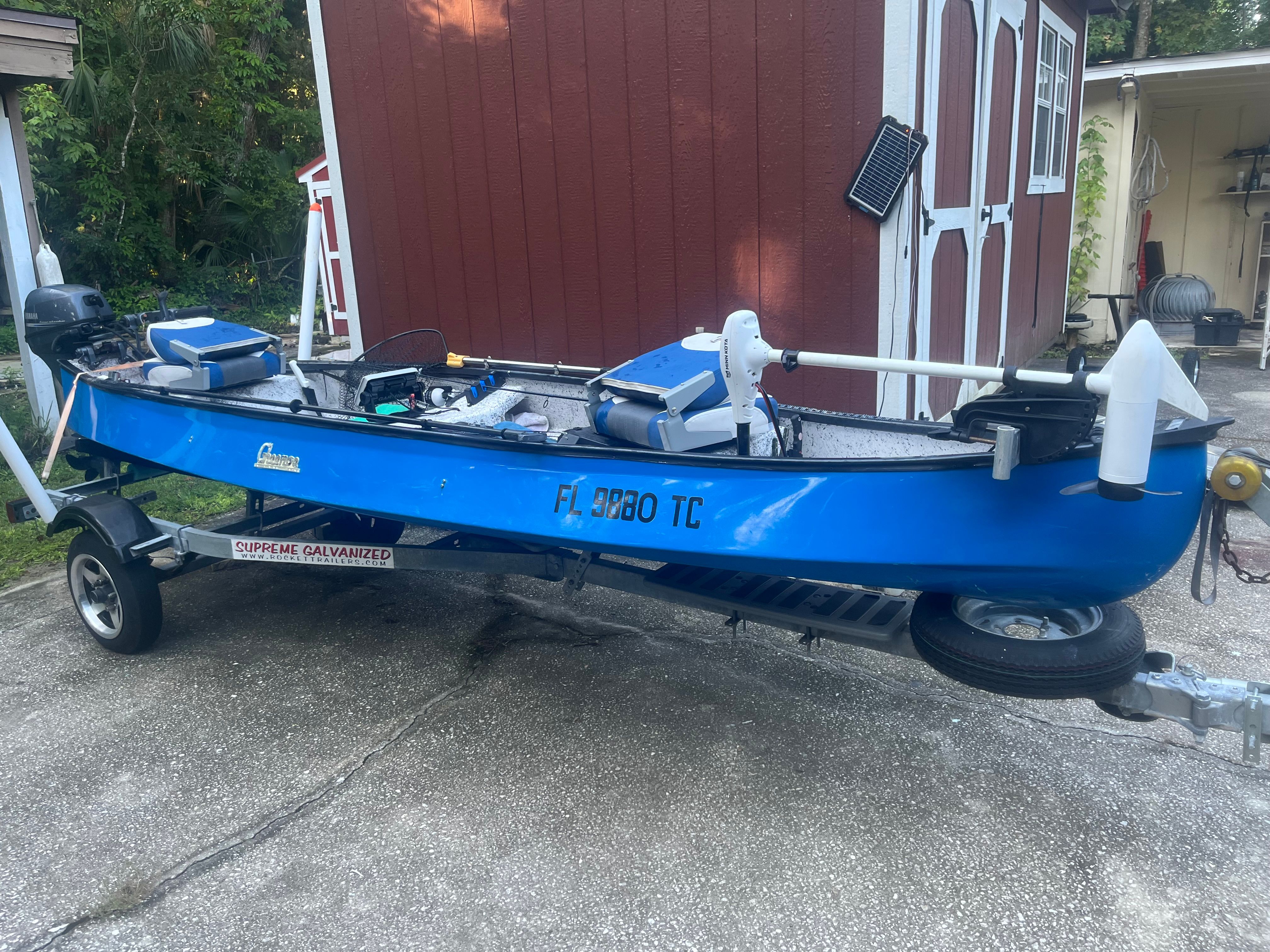 Blue Custom 15-4 boat on trailer, 2021 model, in front of red shed.