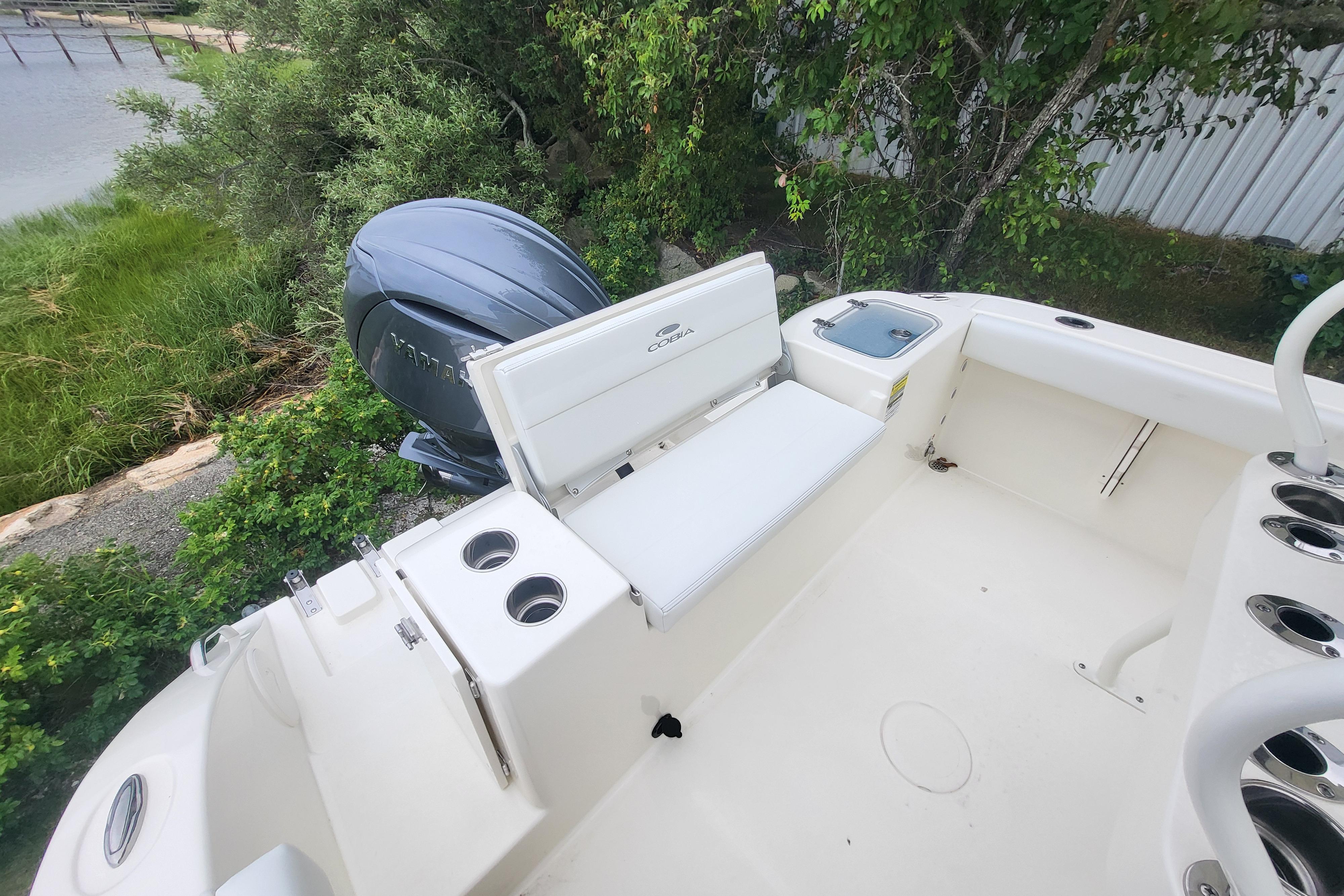2025 Cobia 220 Center Console boat with Yamaha engine, docked near lush greenery.