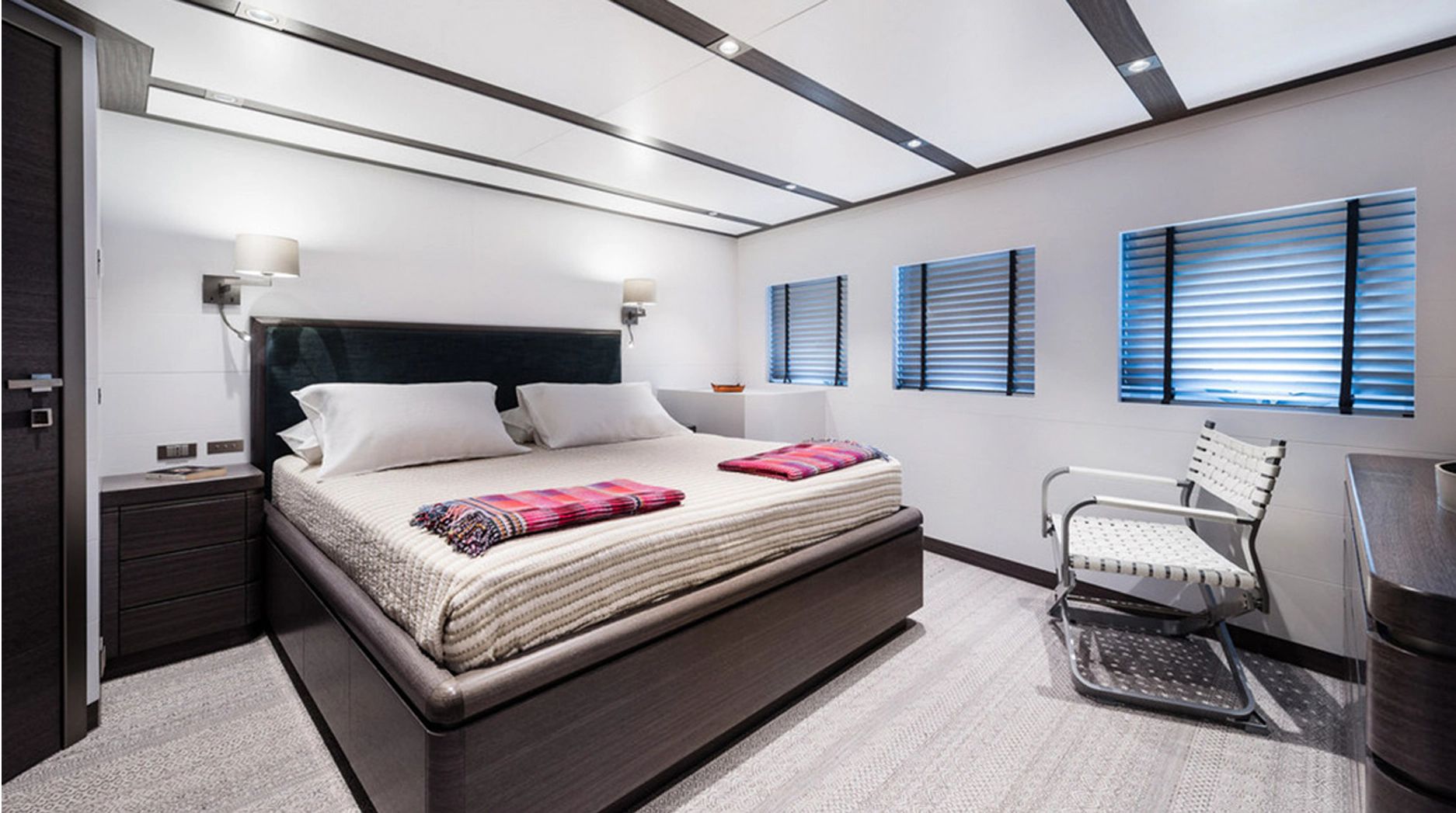 Luxurious bedroom with a large bed, modern furniture, and several windows.